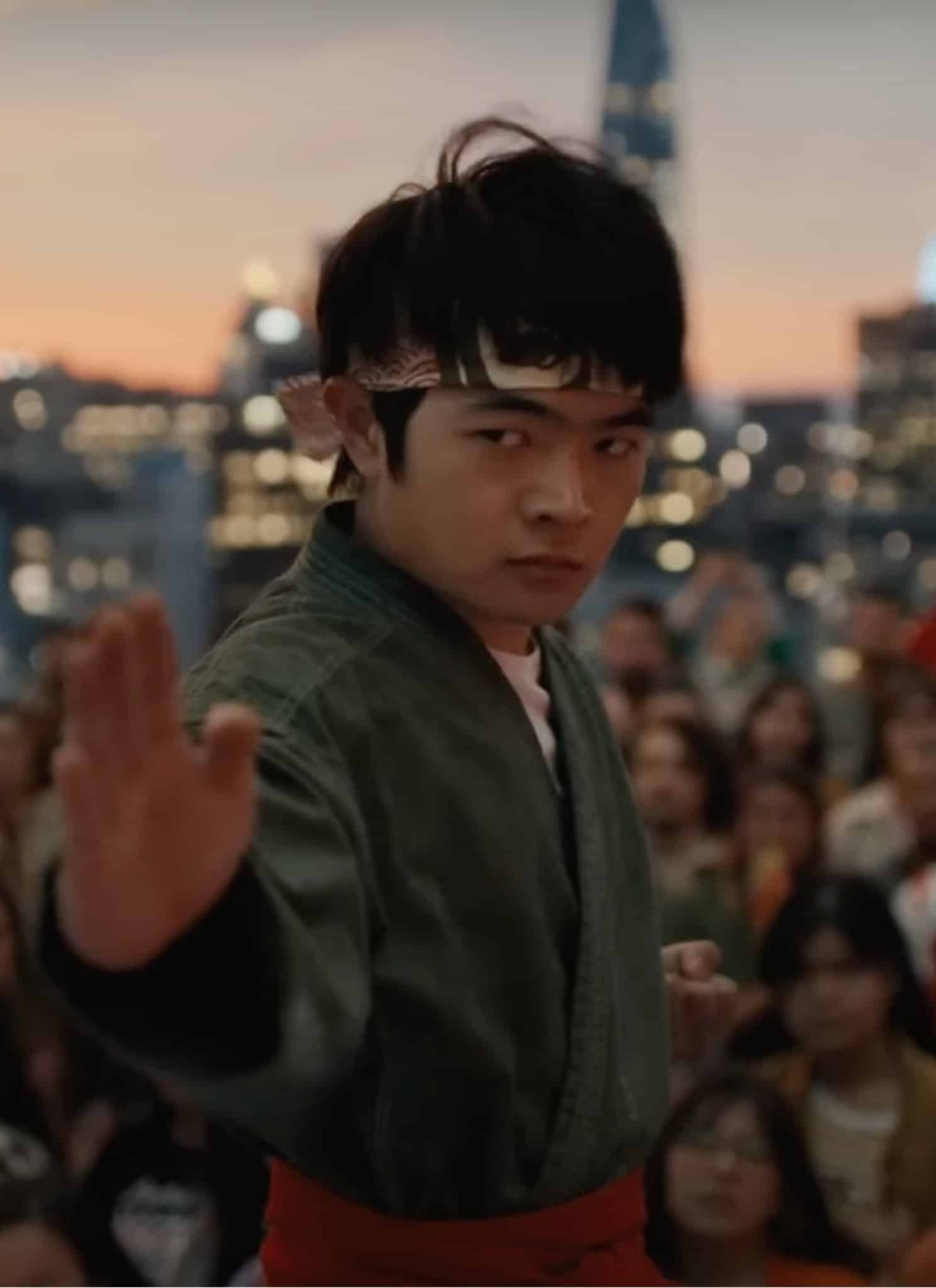 Ben Wang as Li Fong in gray karate gi striking a pose with crowd in the background.
