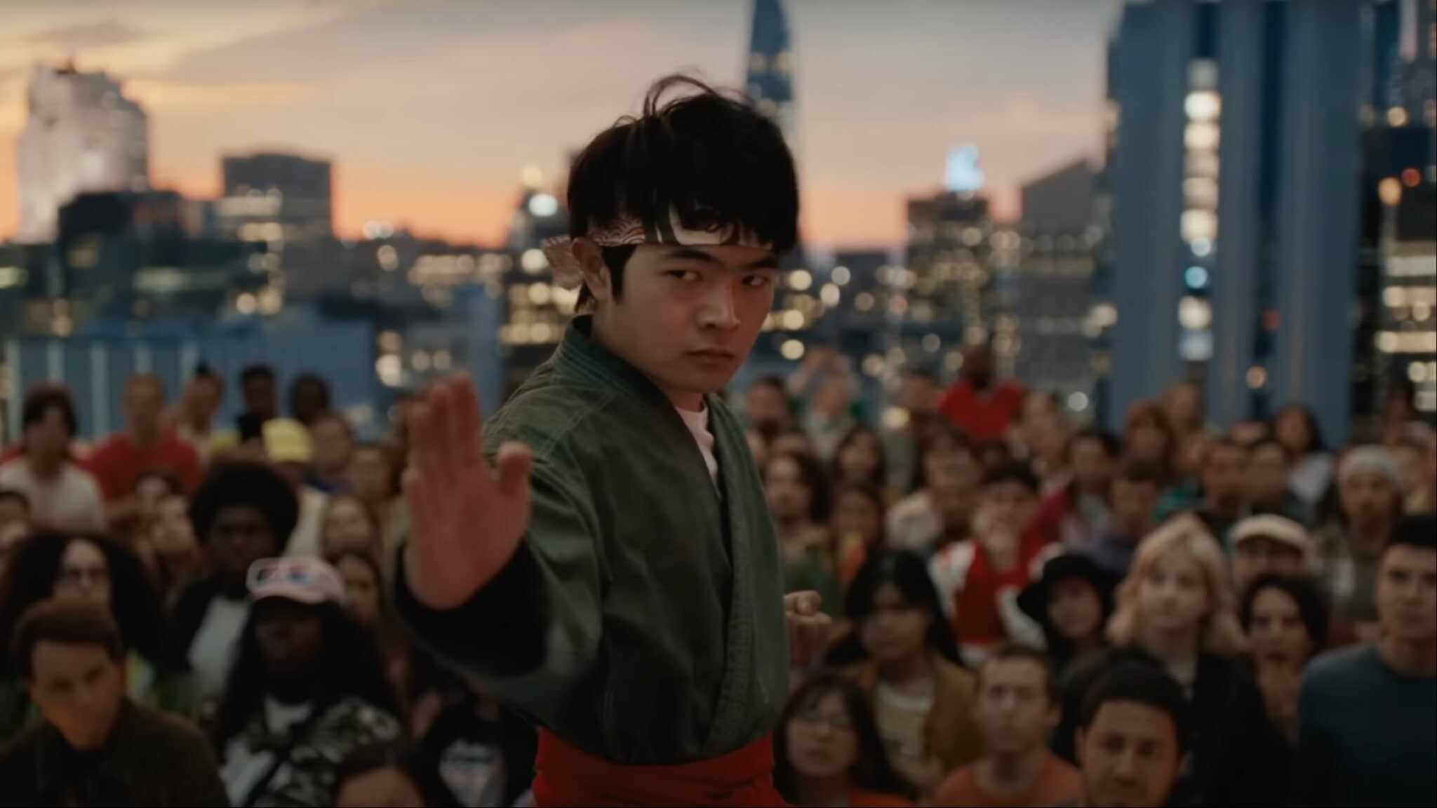 Ben Wang as Li Fong in gray karate gi striking a pose with crowd in the background.