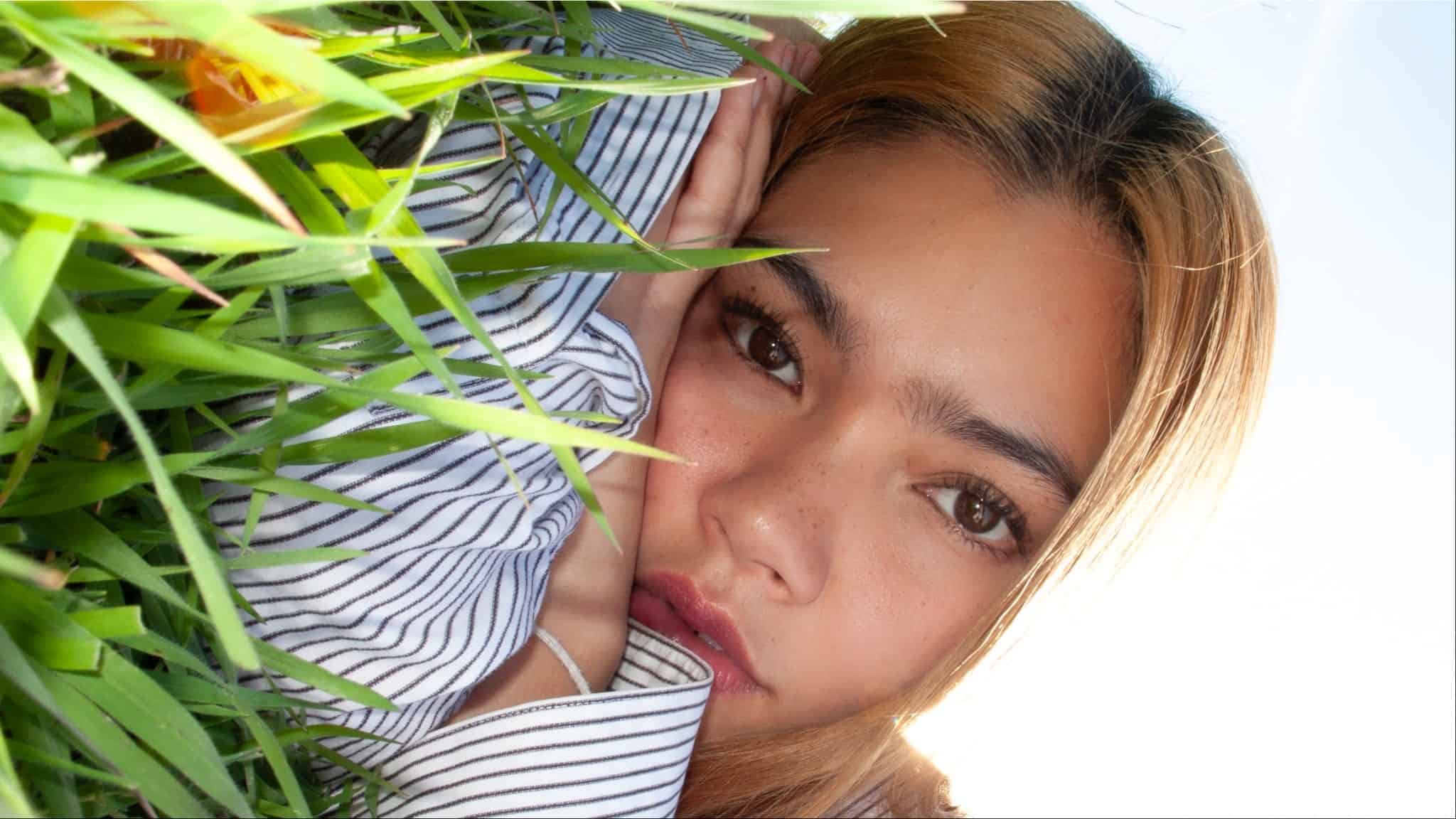 Myra Molloy wearing blue stripe shirt lying in grass.
