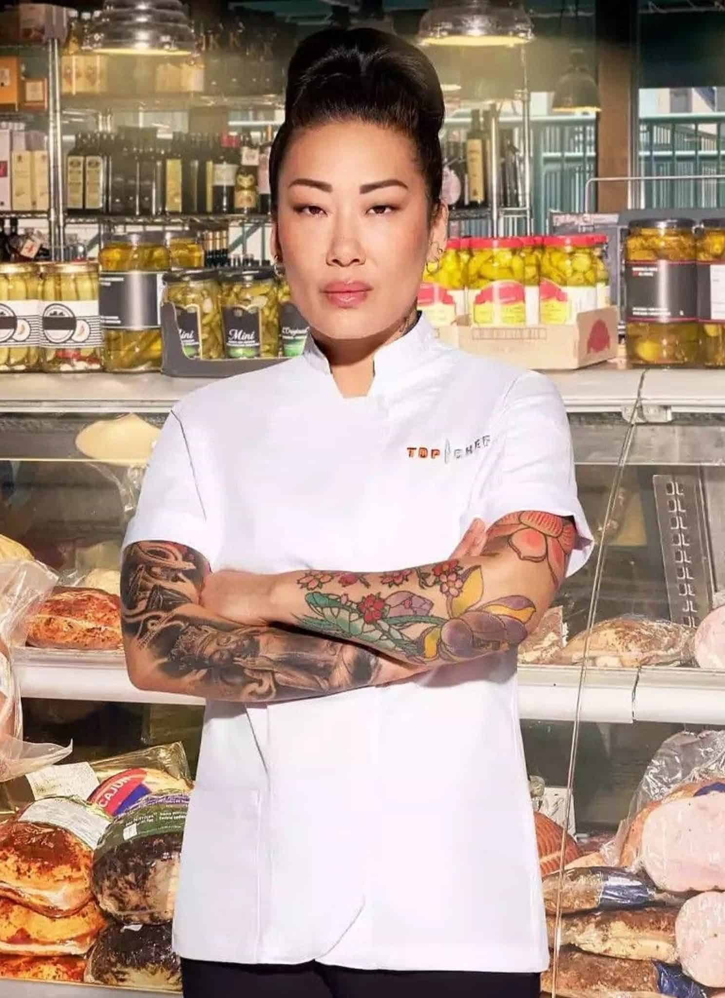 Katianna Hong in white chef jacket standing in front of deli counter.