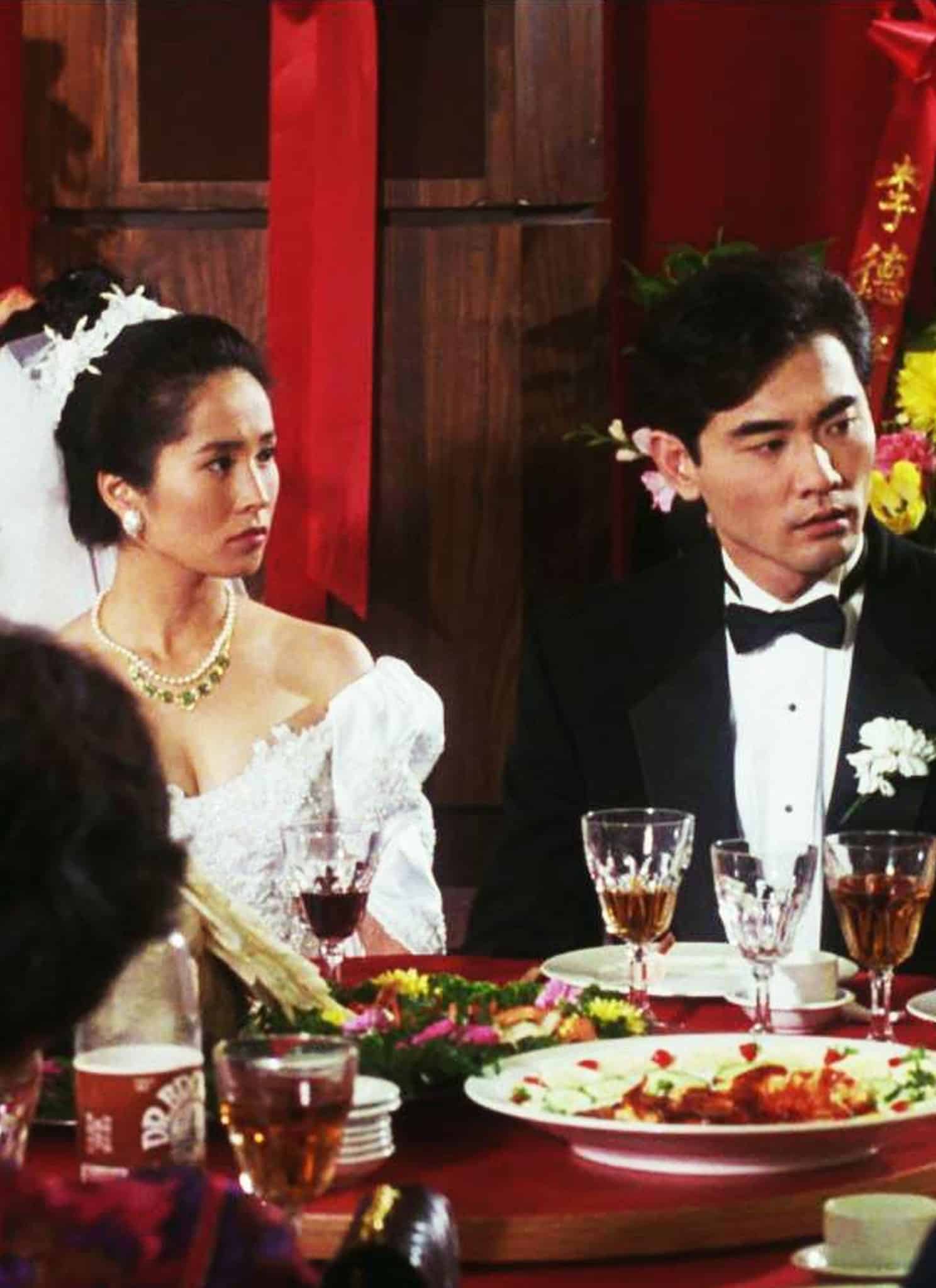 Still from Ang Lee's "The Wedding Banquet"; a couple in wedding outfits sit at a table with others.