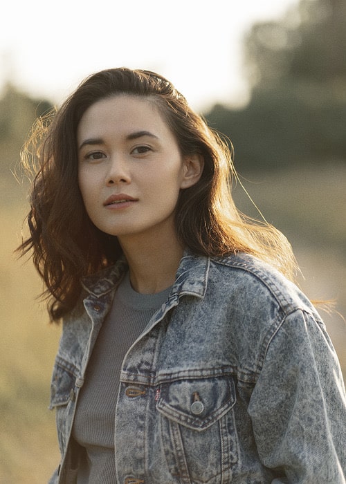 Mixed Asian actress Chelsea Muirhead, in a denim jacket and gray top, against a blurred background.