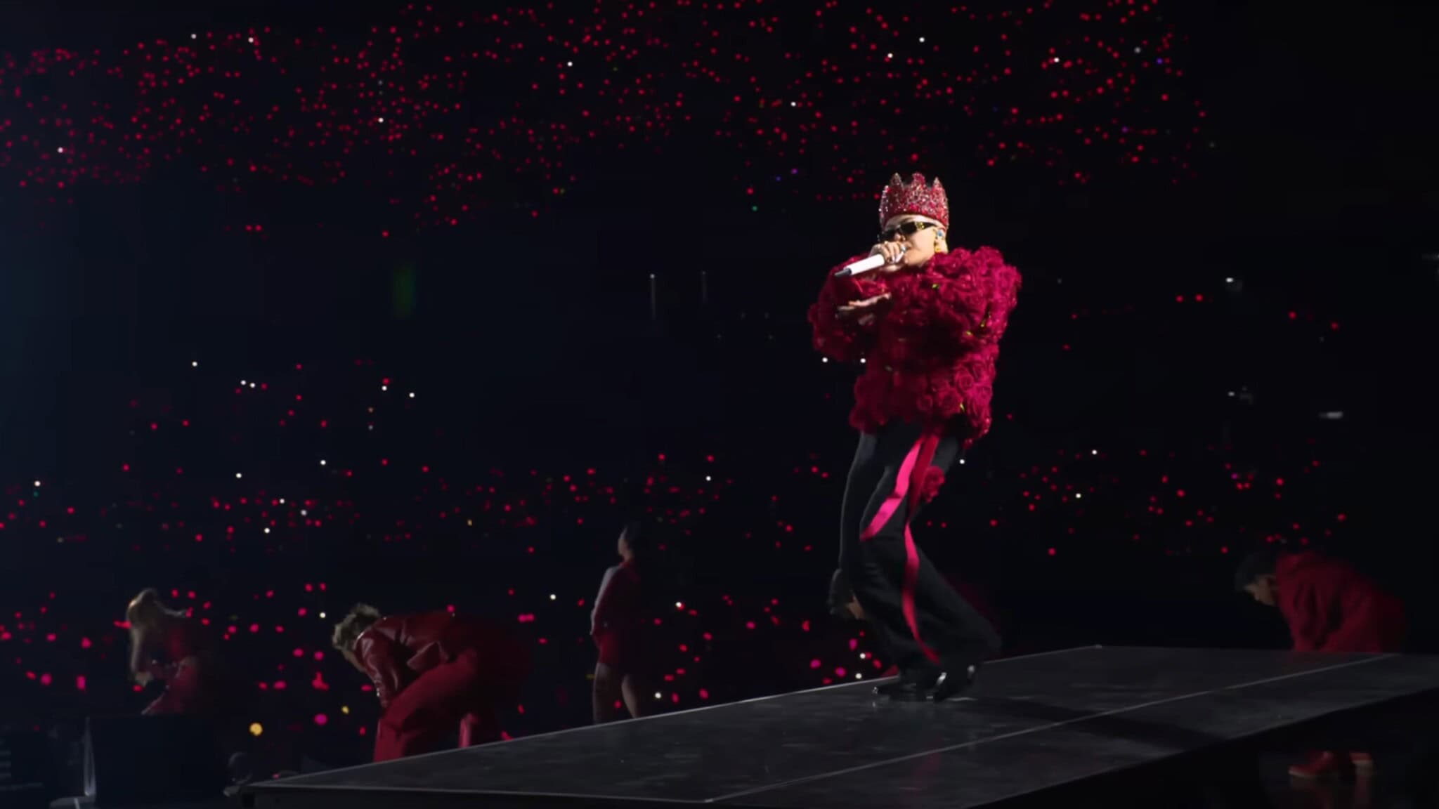 K-pop artist G-Dragon performs on stage in a red top, black pants and red crown.