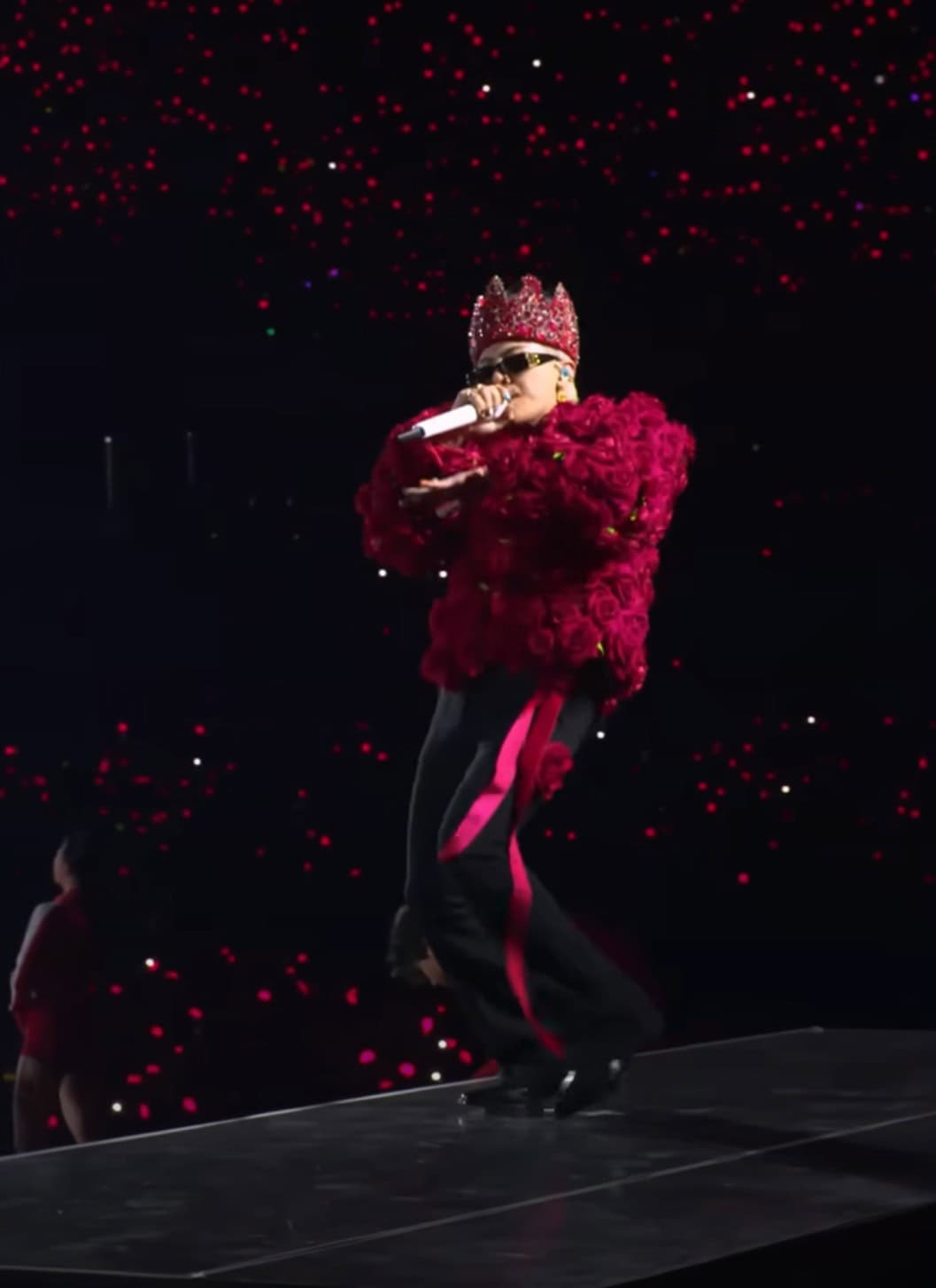 K-pop artist G-Dragon performs on stage in a red top, black pants and red crown.