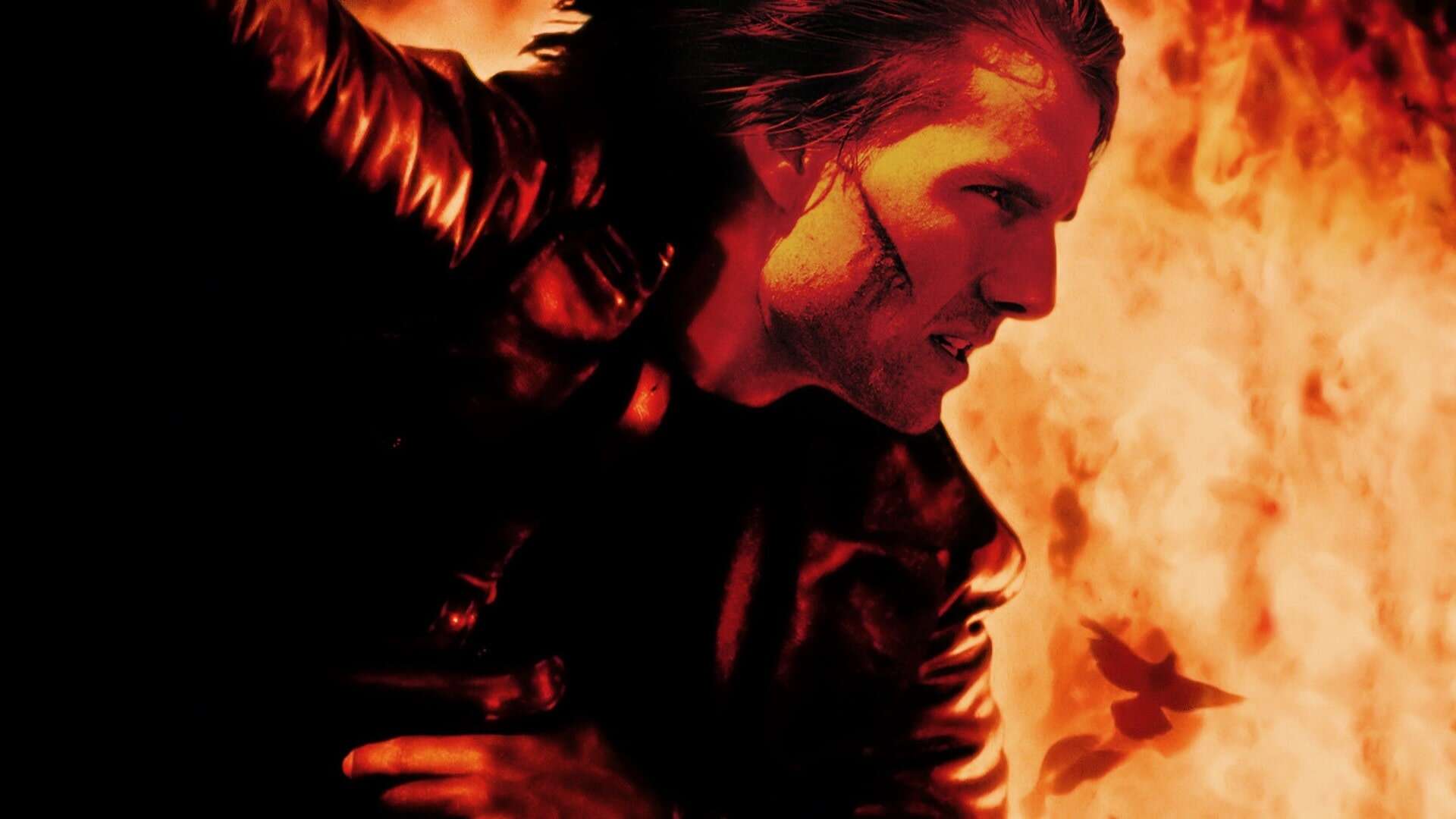 A closeup of actor Tom Cruise, with orange flames in the background.