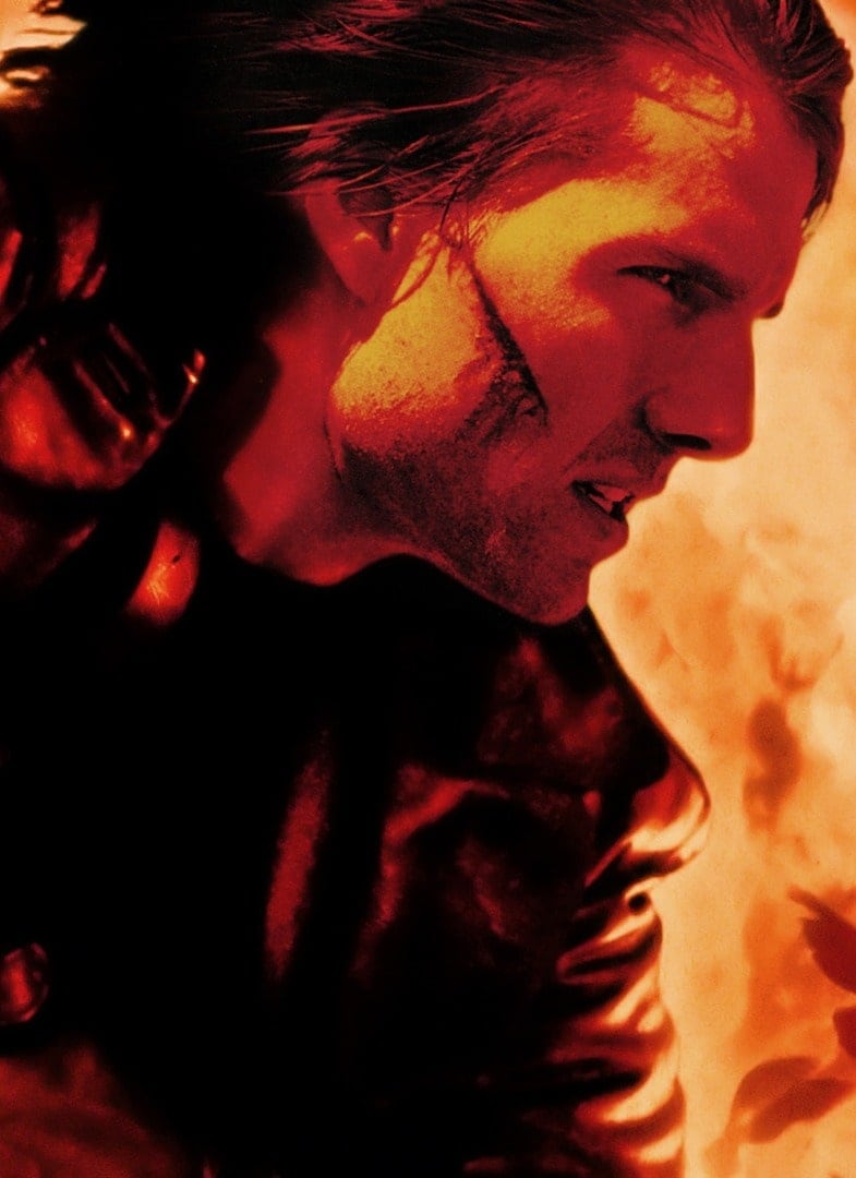 A closeup of actor Tom Cruise, with orange flames in the background.