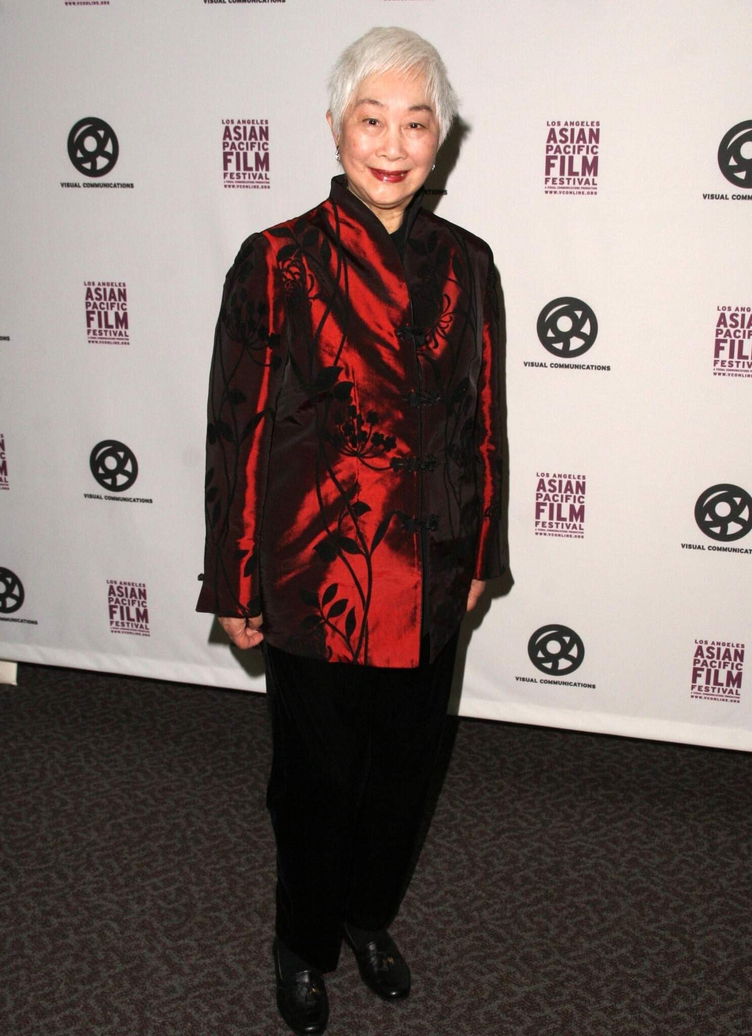 Lisa Lu standing in front of backdrop in red and black outfit.