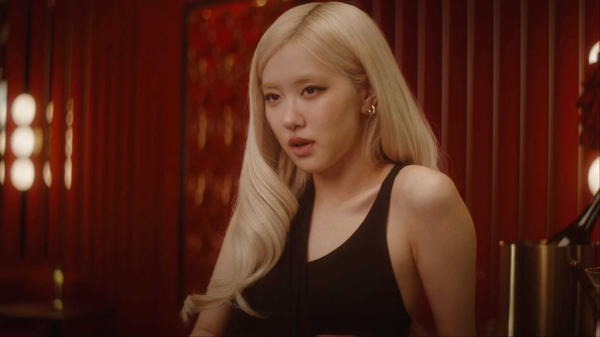 Rosé singing and sitting in red room wearing black top.