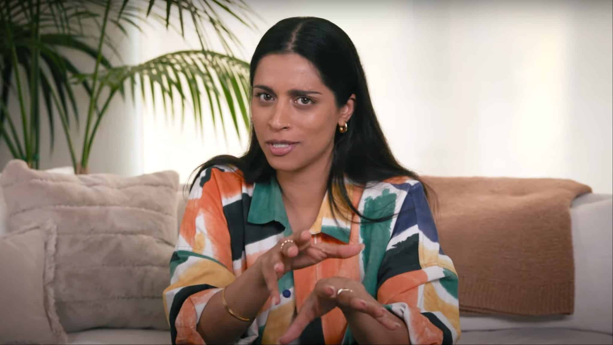 Lilly Singh in colorful shirt sitting on couch.