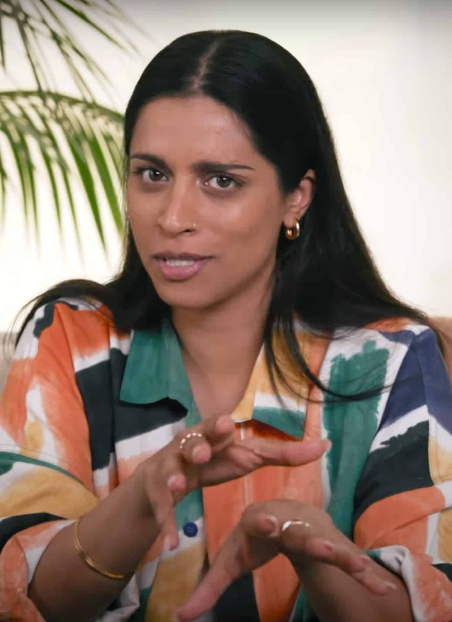 Lilly Singh in colorful shirt sitting on couch.