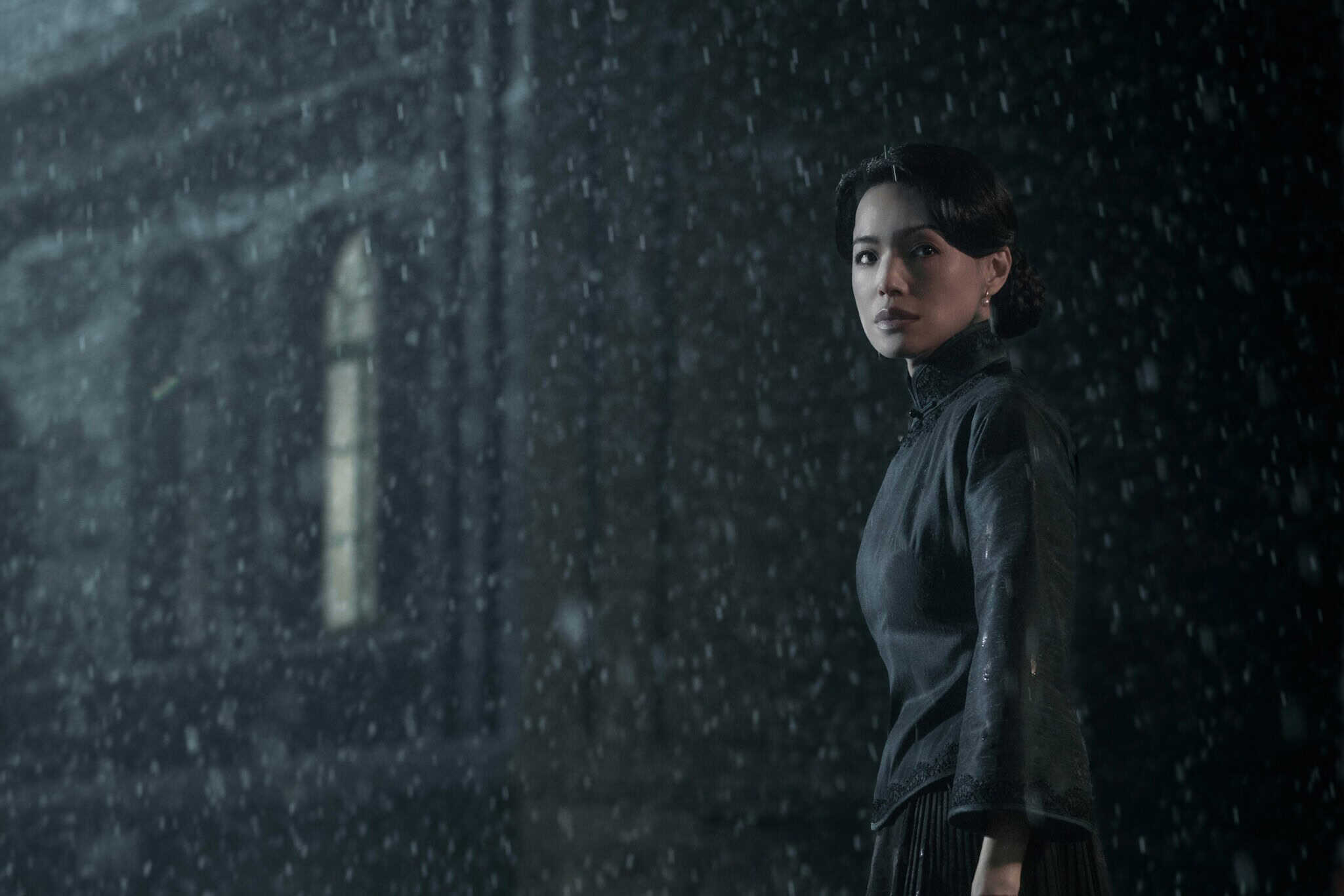 Chinese actress Shu Qi, dressed in black, stands in the rain in front of a dark building.