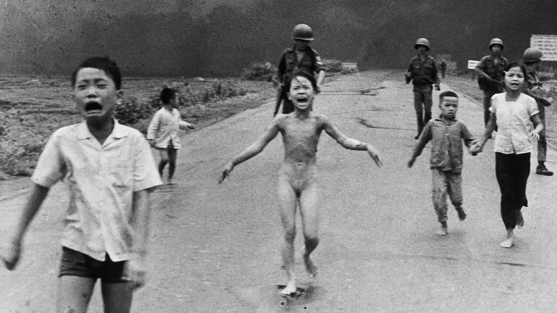 Vietnamese children and soldiers run down a road, one girl is naked and crying.
