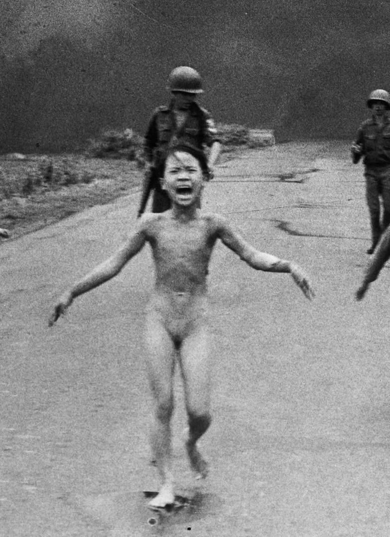 Vietnamese children and soldiers run down a road, one girl is naked and crying.