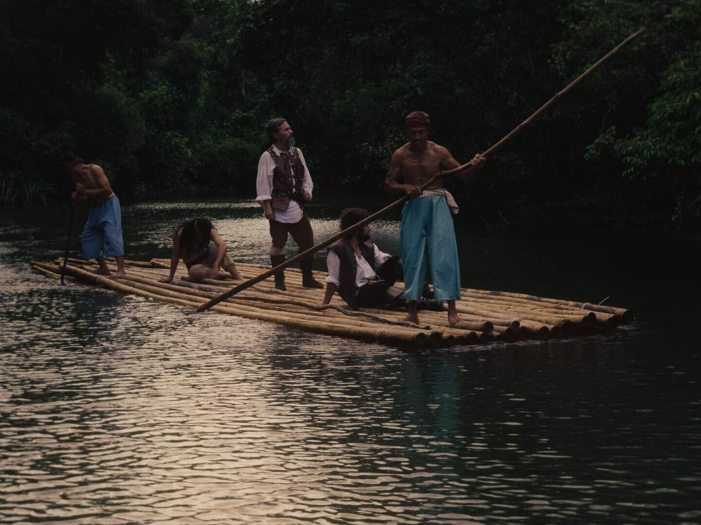 Still from "Magellan"; several men stand on a raft in the water.