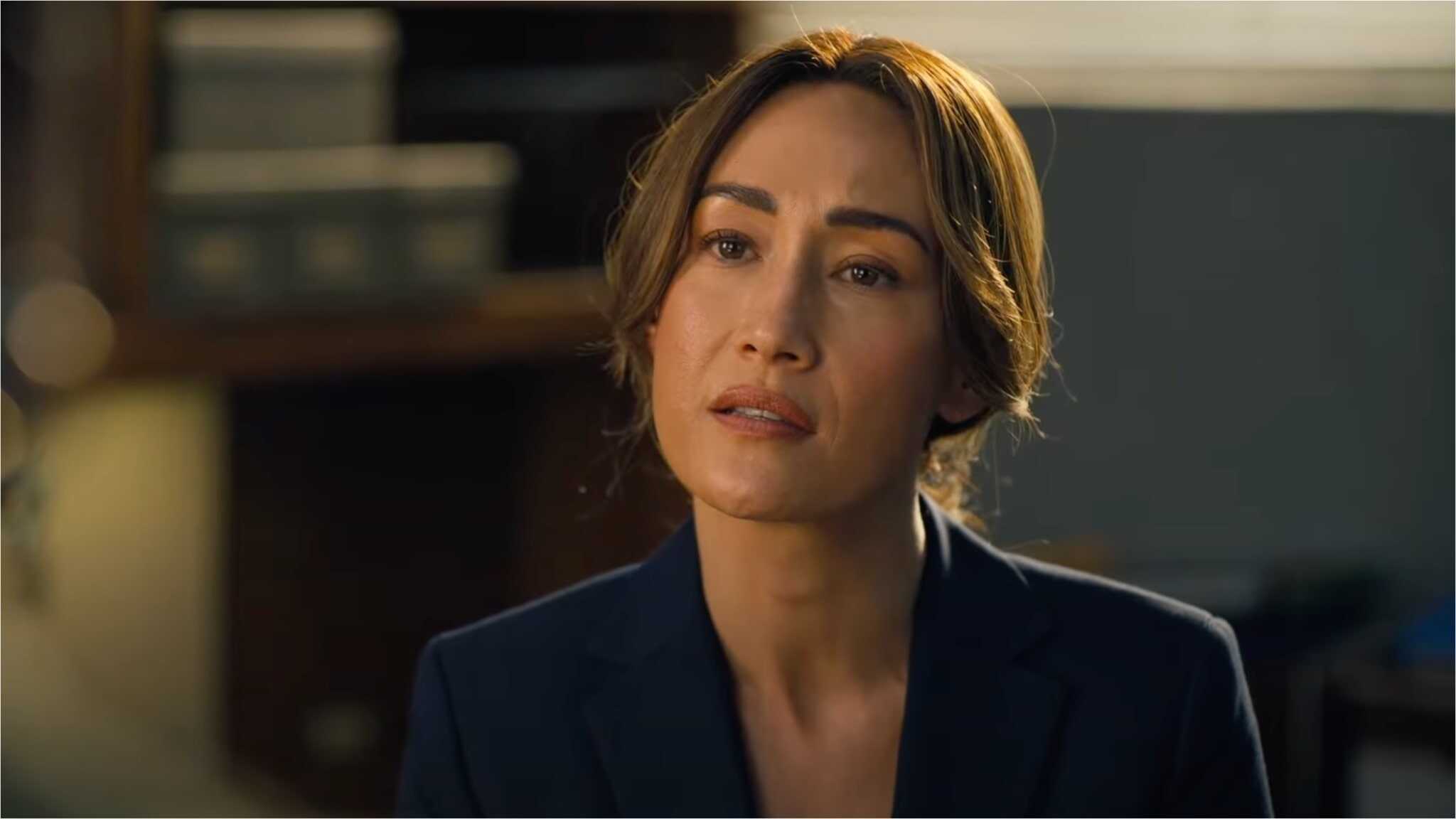 Maggie Q in blue black blazer sitting in office.