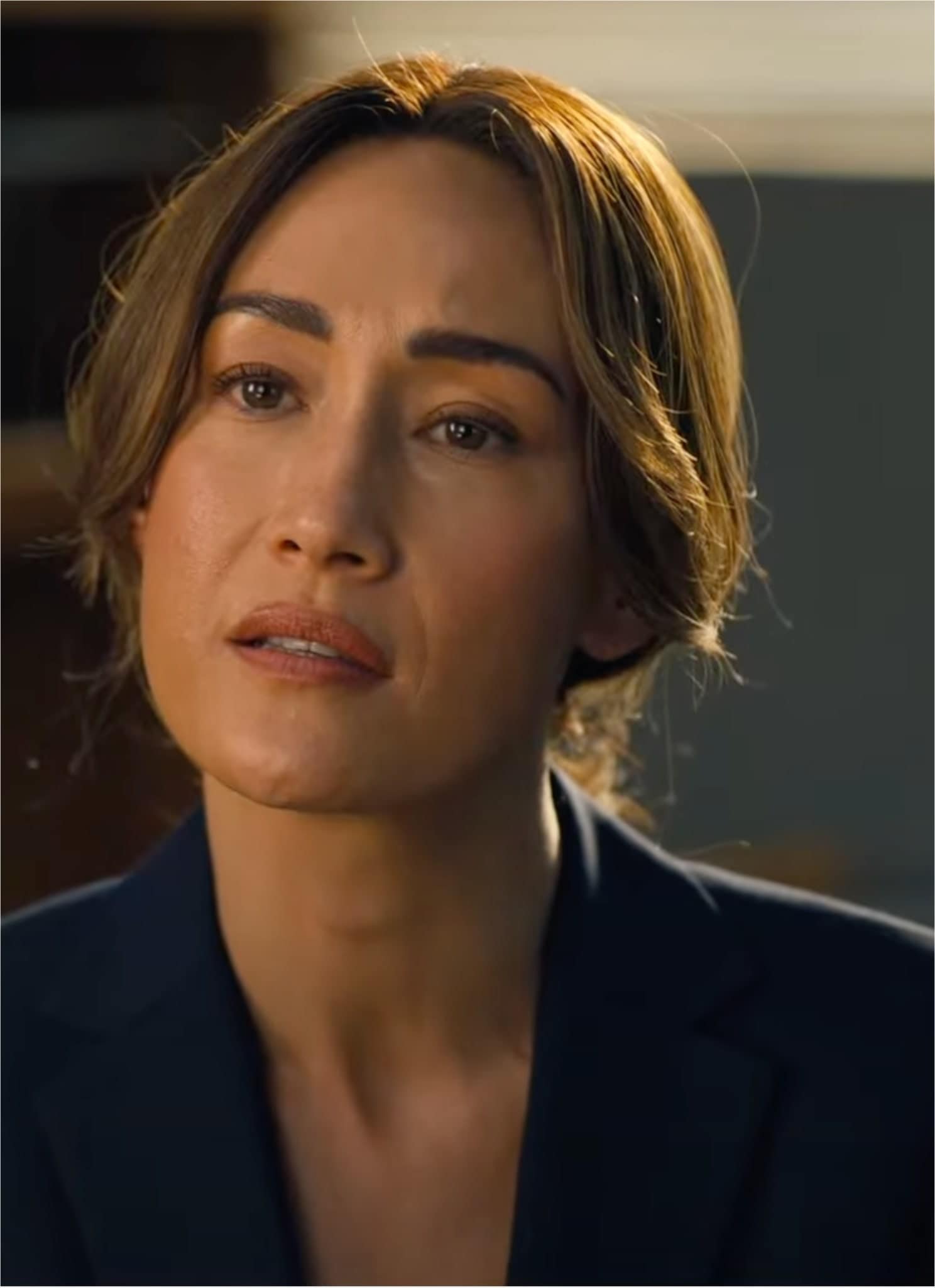 Maggie Q in blue black blazer sitting in office.