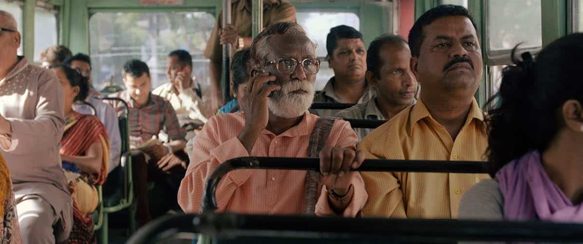 Several south Asian people sit on a bus, with one man in glasses and a white beard holding a cell phone to his ear, in "Court."