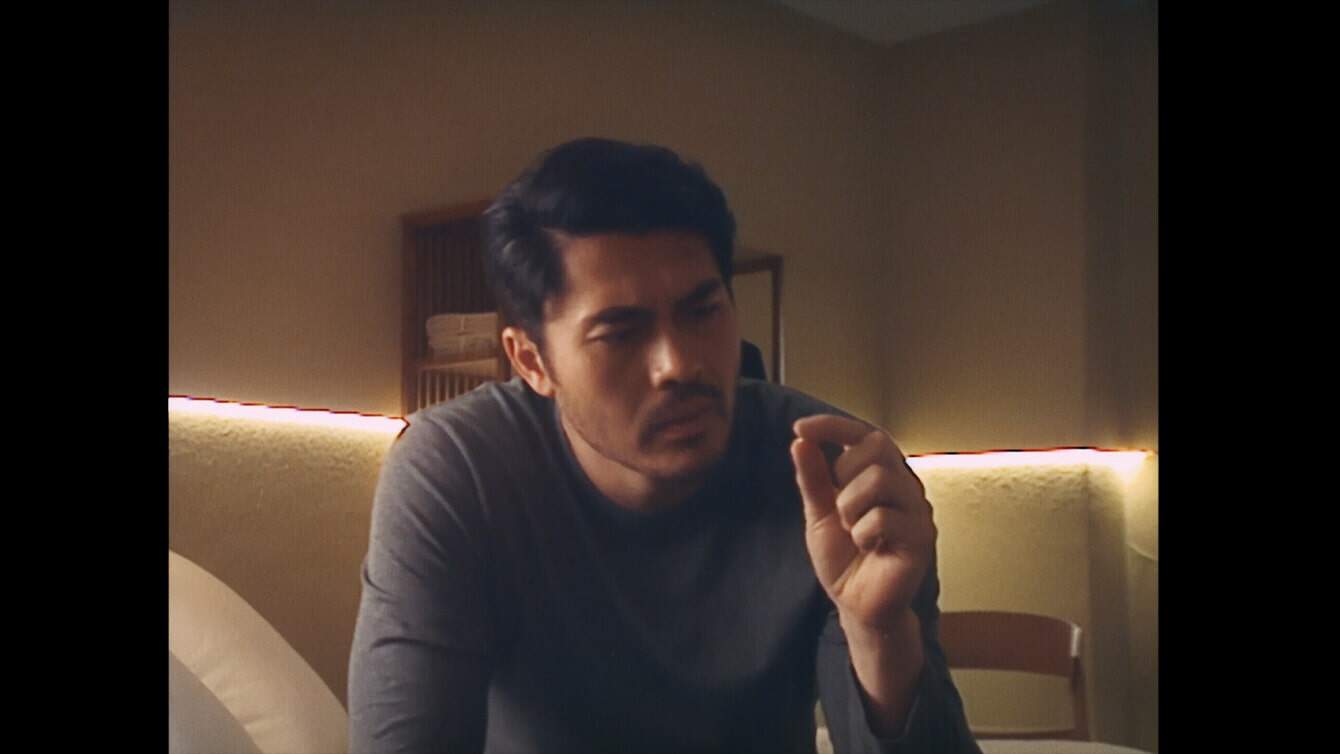 Henry Golding in gray shirt looking at pill. 