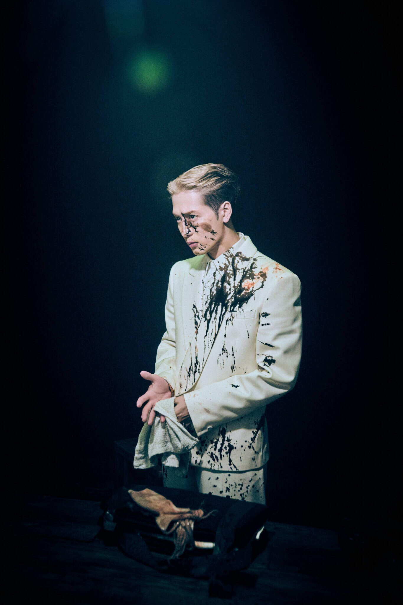 Singer Jackson Wang in a white suit, with black ink splashed on his body and face.