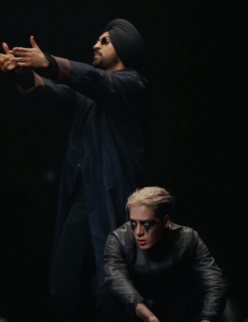 Music artists Diljit Dosanjh and Jackson Wang, dressed in black against a black background.