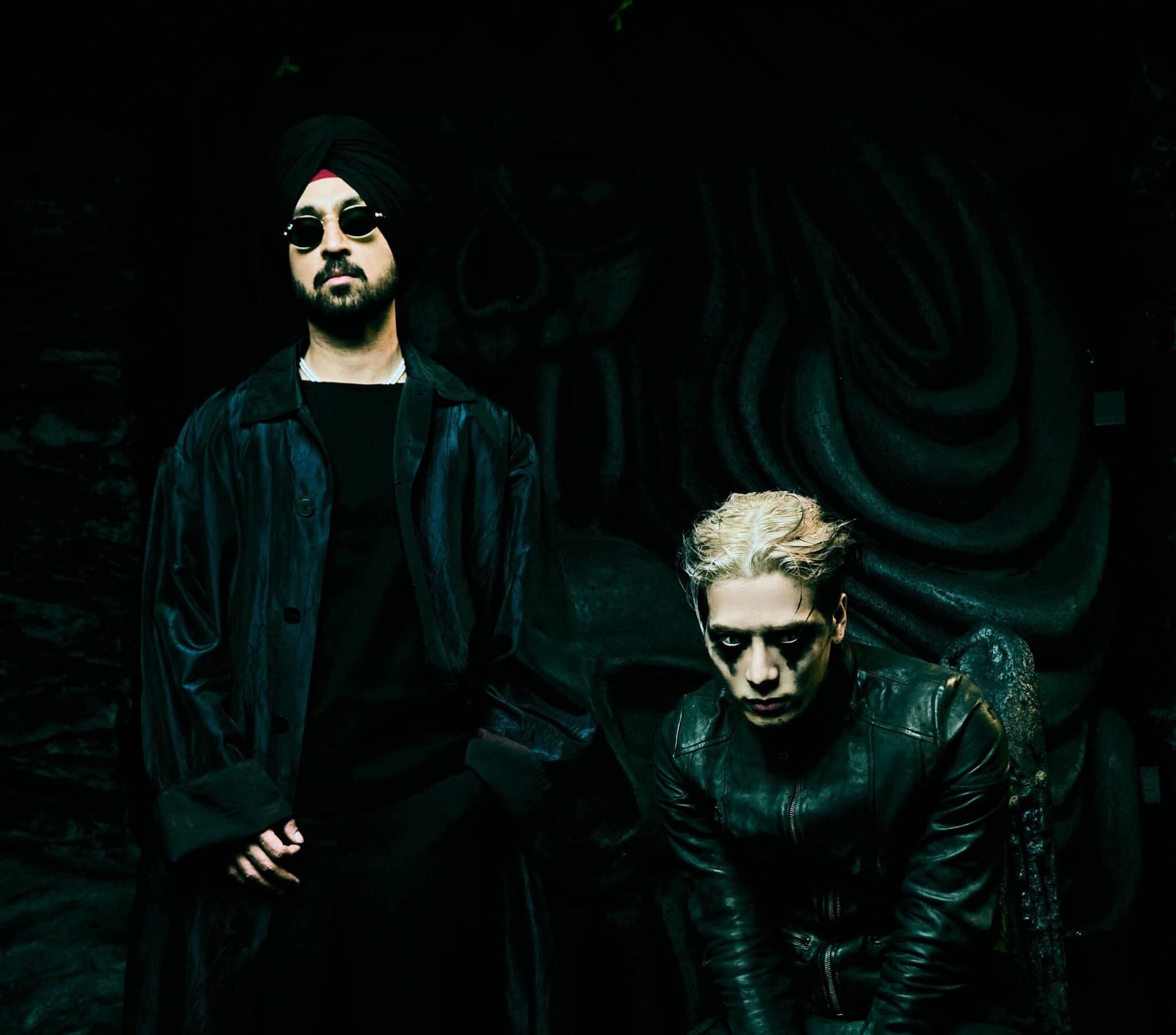 Music artists Diljit Dosanjh and Jackson Wang, dressed in black against a black background.