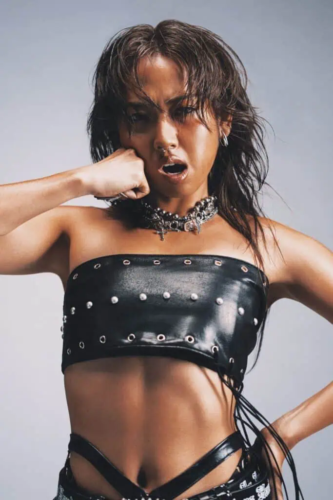 MILLI in a black outfit, her hand in a fist touching her own face.