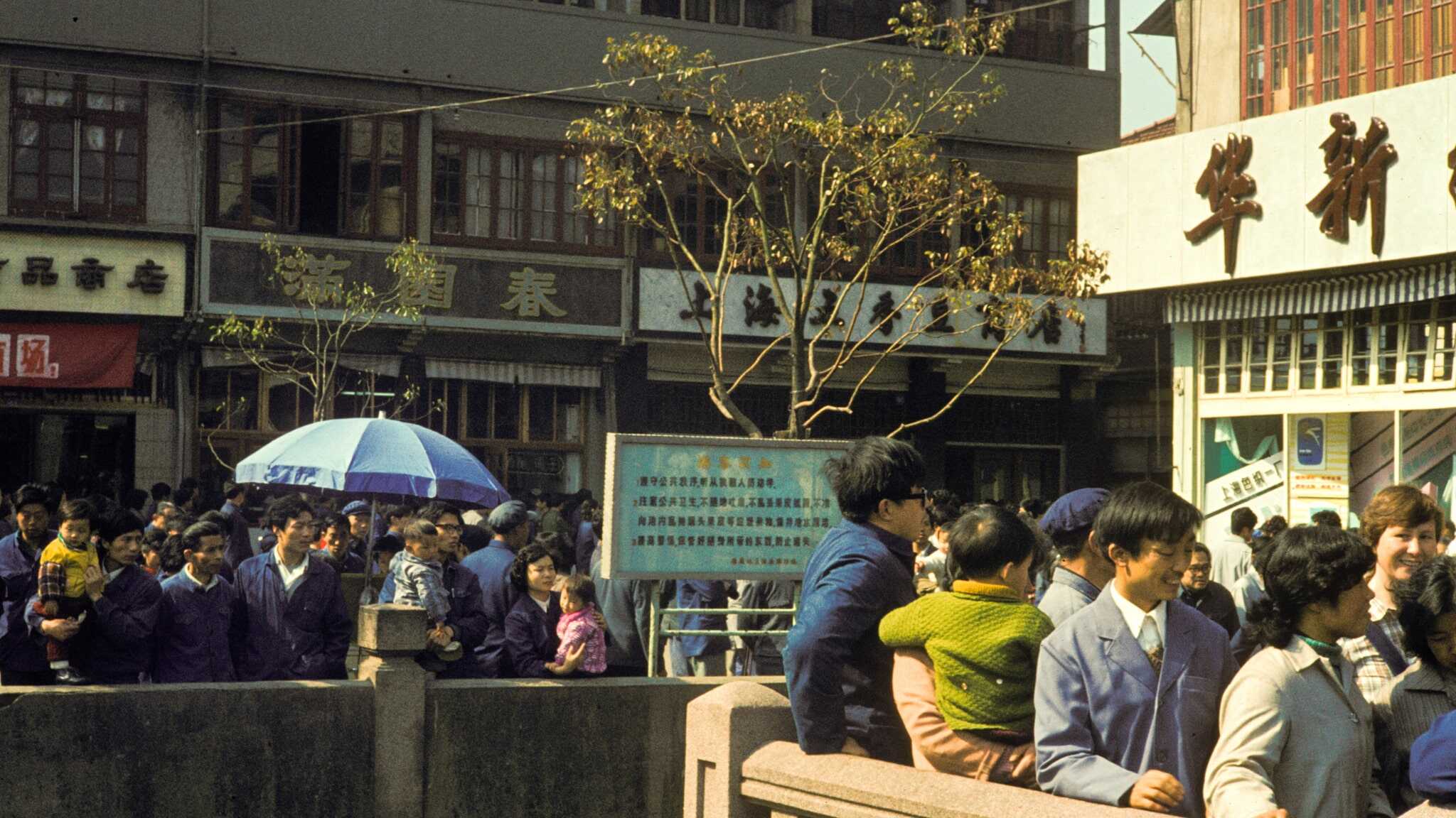 A group of Chinese people stand outside business buildings against a stone railing in China in 1982.