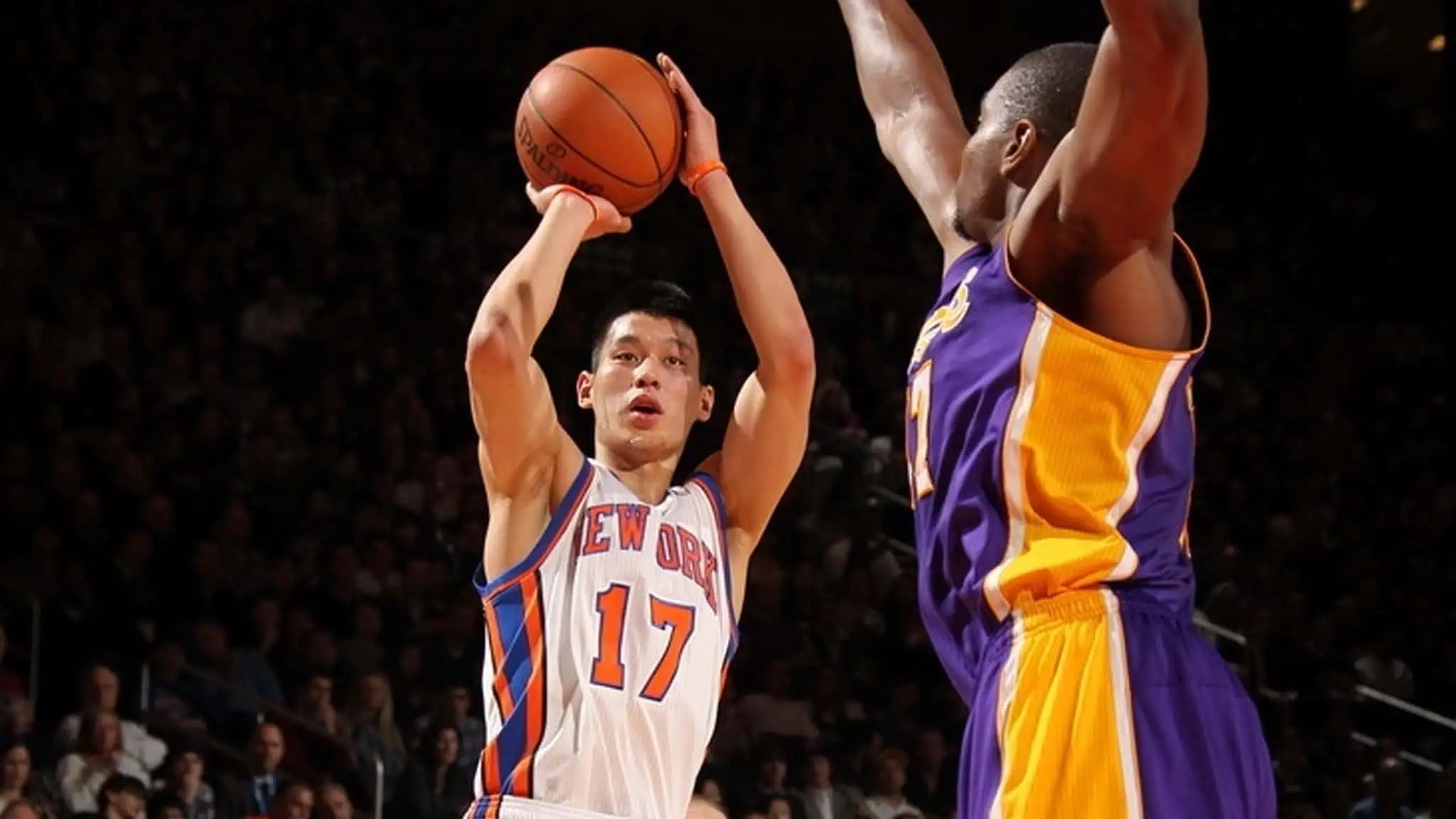 A basketball player in a New York Knicks jersey, number 17, jumps to shoot the ball as a Los Angeles Lakers defender raises his arms to block the shot during a game.