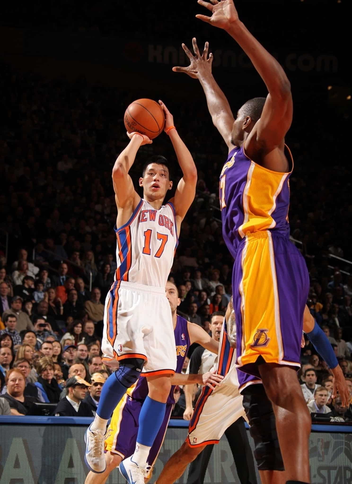 A basketball player in a New York Knicks jersey, number 17, jumps to shoot the ball as a Los Angeles Lakers defender raises his arms to block the shot during a game.