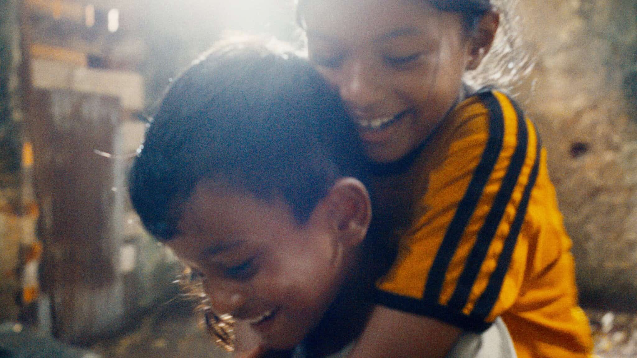 Two children smiling and playing together indoors, with one child giving the other a piggyback ride. The scene is brightly lit and joyful, capturing their happiness and close friendship.