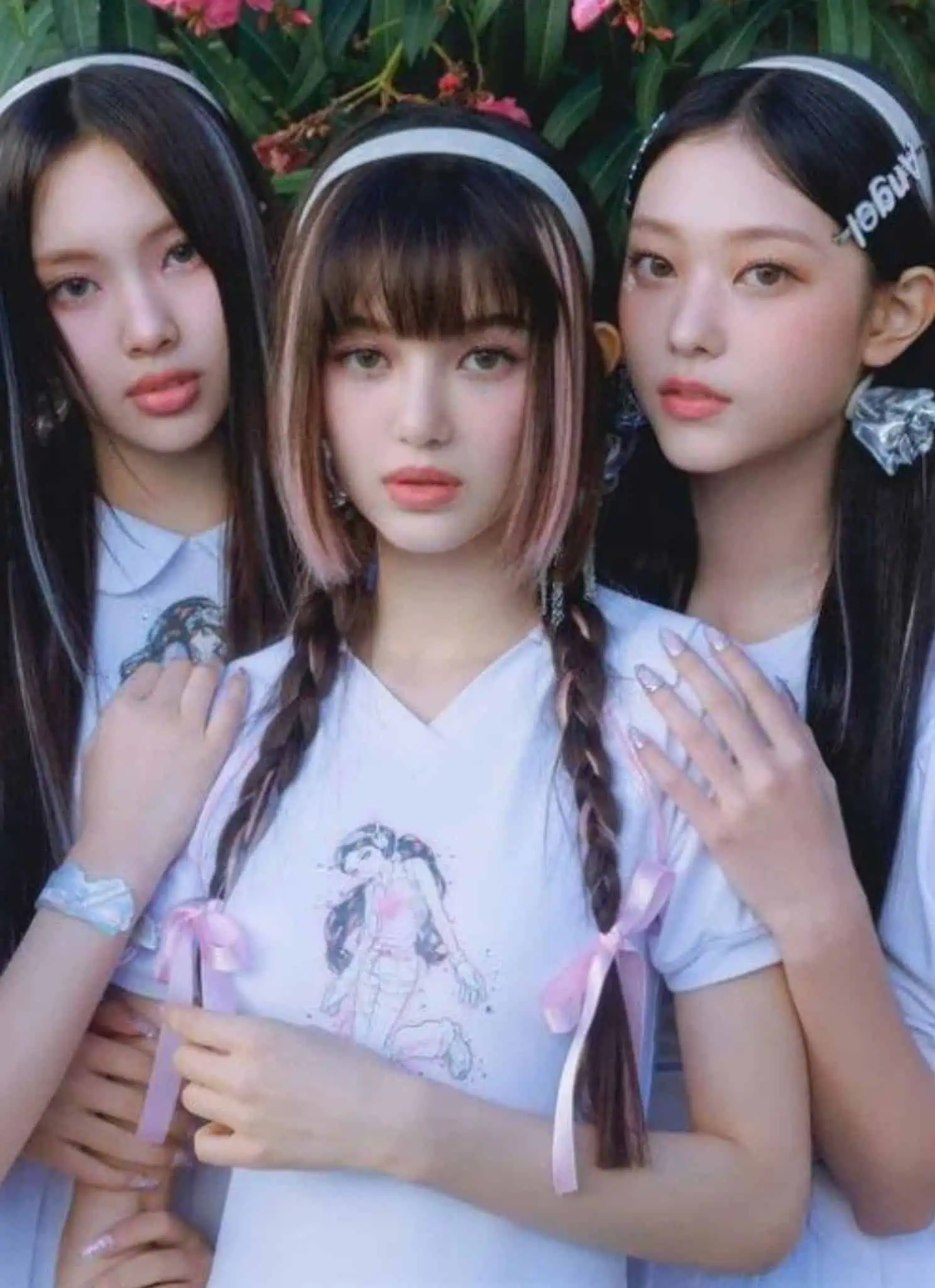 Five young women with long, straight hair and matching white shirts pose closely together outdoors, surrounded by greenery. They wear headbands and have neutral expressions, looking directly at the camera.