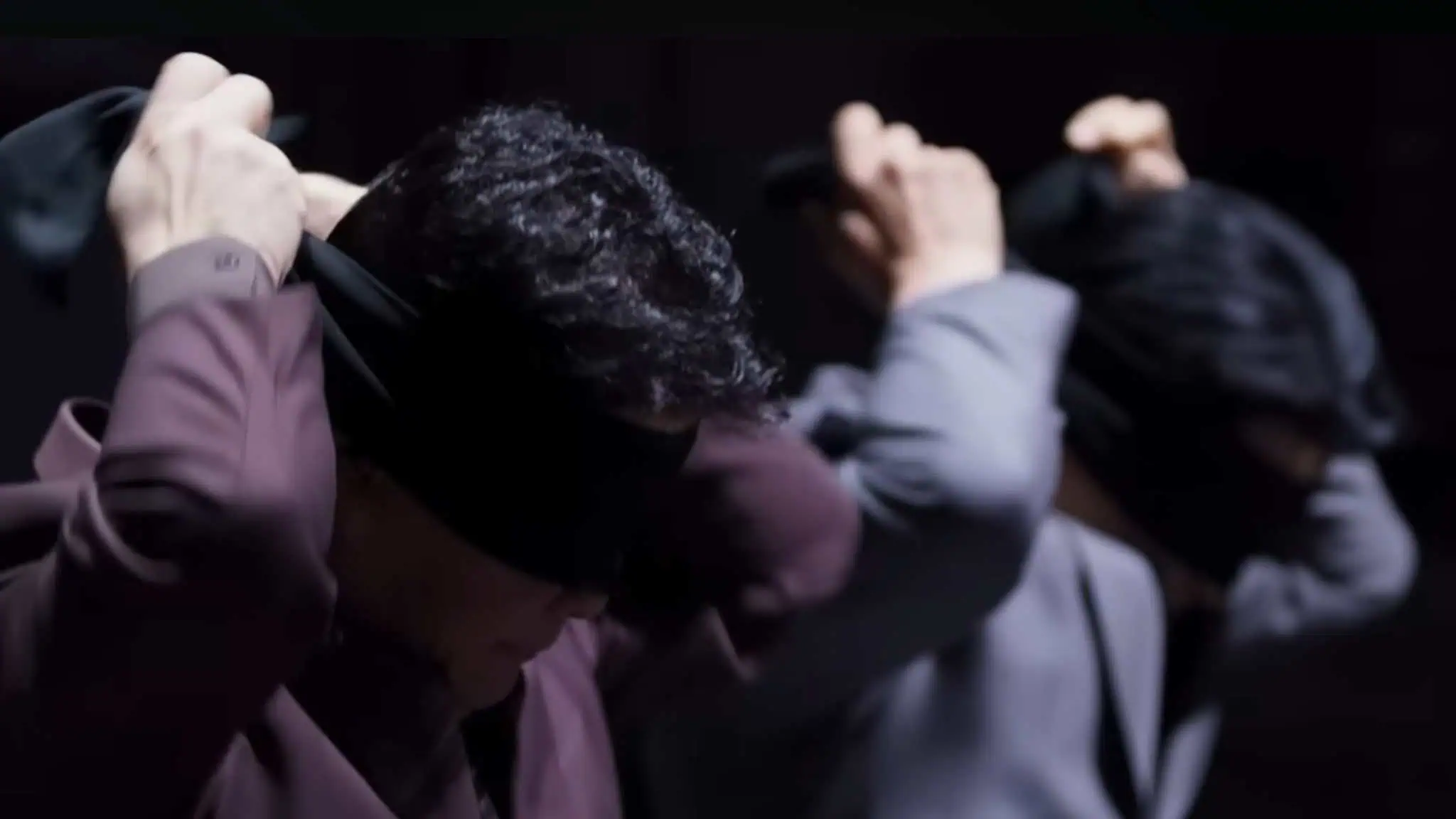 Two people in suits, caught in the intrigue of Culinary Class Wars, put black blindfolds over their eyes, both facing slightly downward in a dimly lit setting.