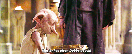 Dobby the house-elf looks happily at a sock in his hands, with the subtitle “Master has given Dobby a sock!” as a person stands nearby, from a scene in the Harry Potter film series.