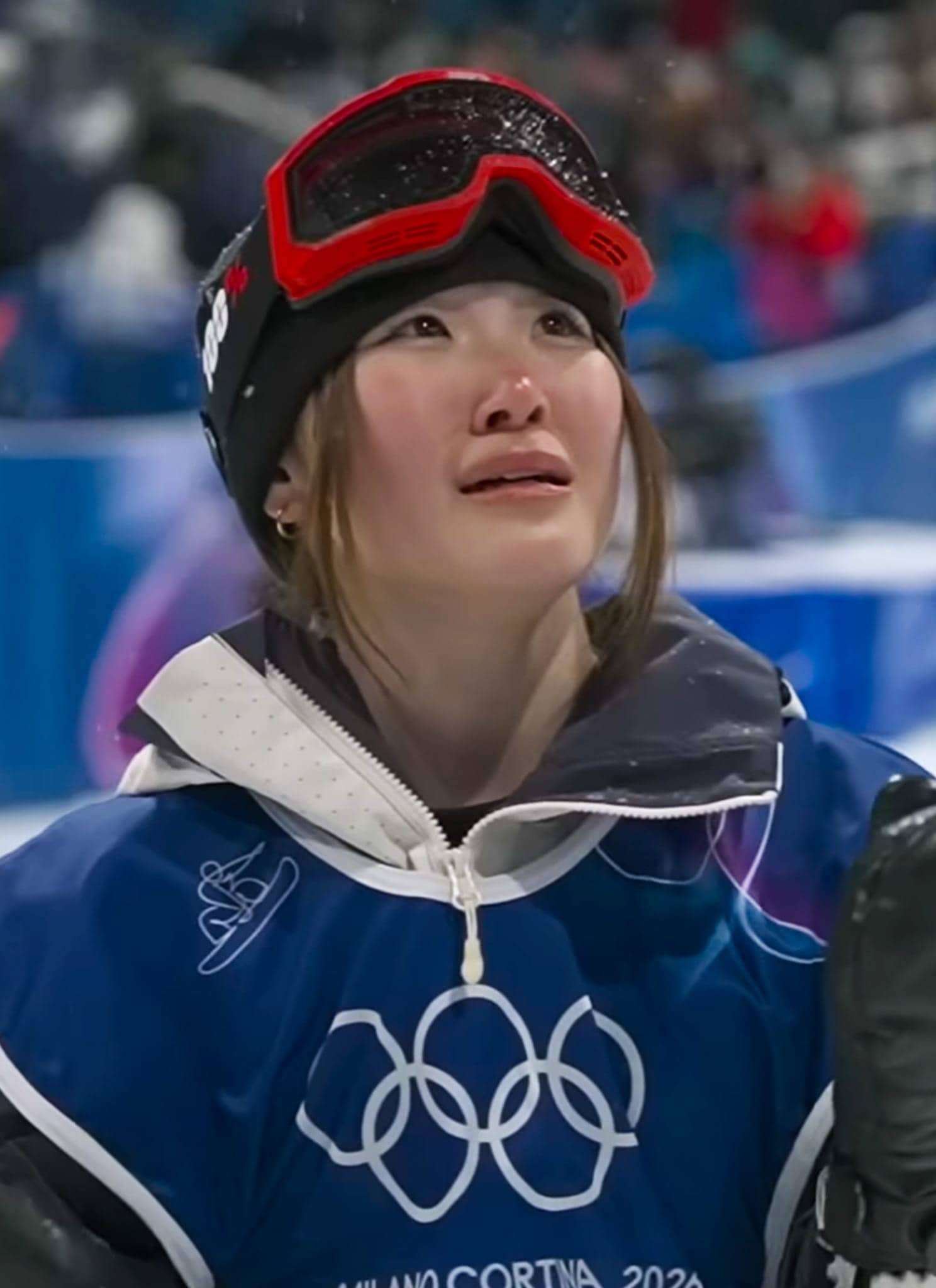 A woman wearing a blue jacket and black hat with red goggles.