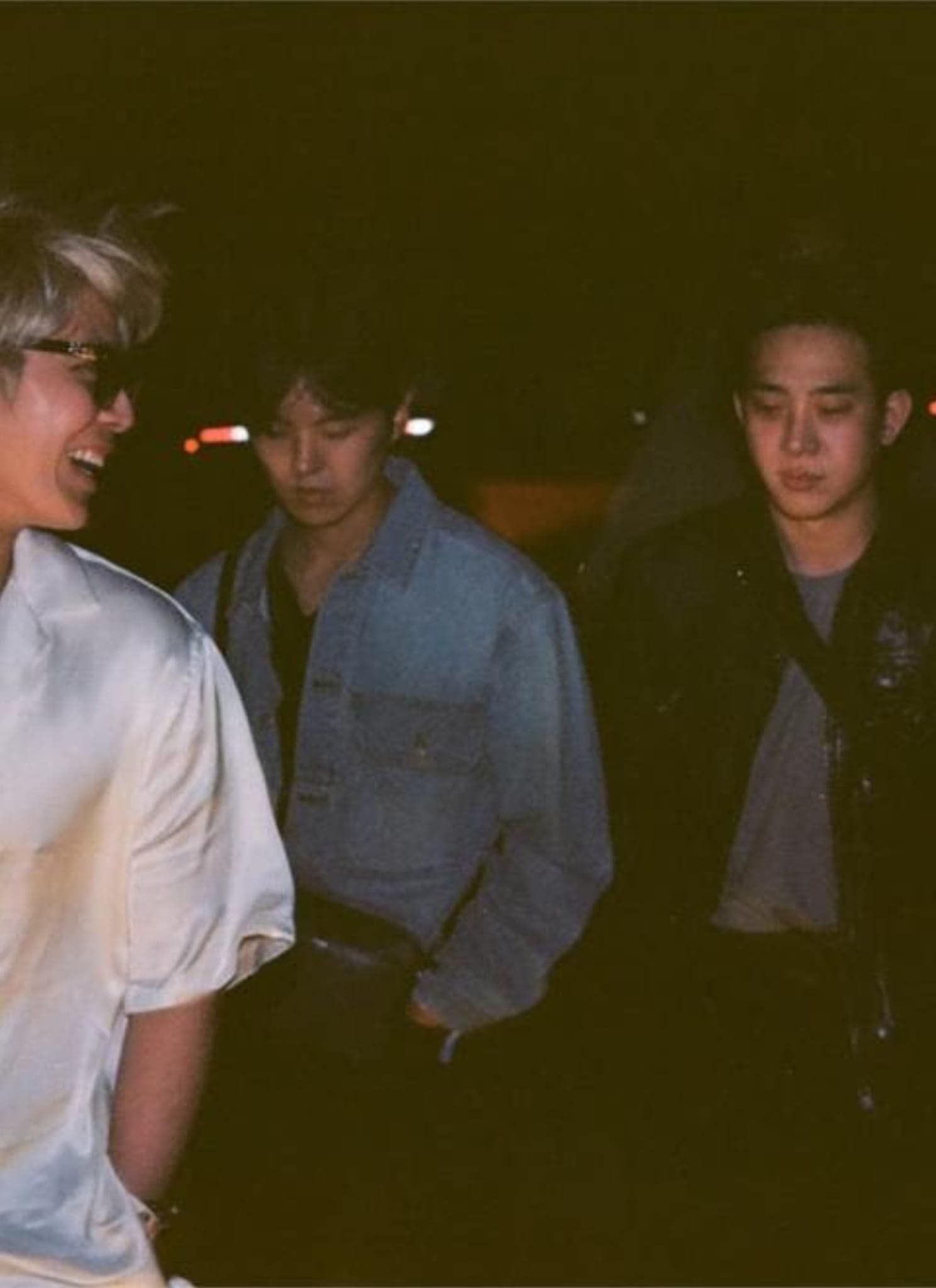 Four young men walk together at night, talking and smiling under dim lighting. Two wear white shirts, one wears a light denim jacket, and one sports a dark jacket—reminiscent of The Rose's effortless style.