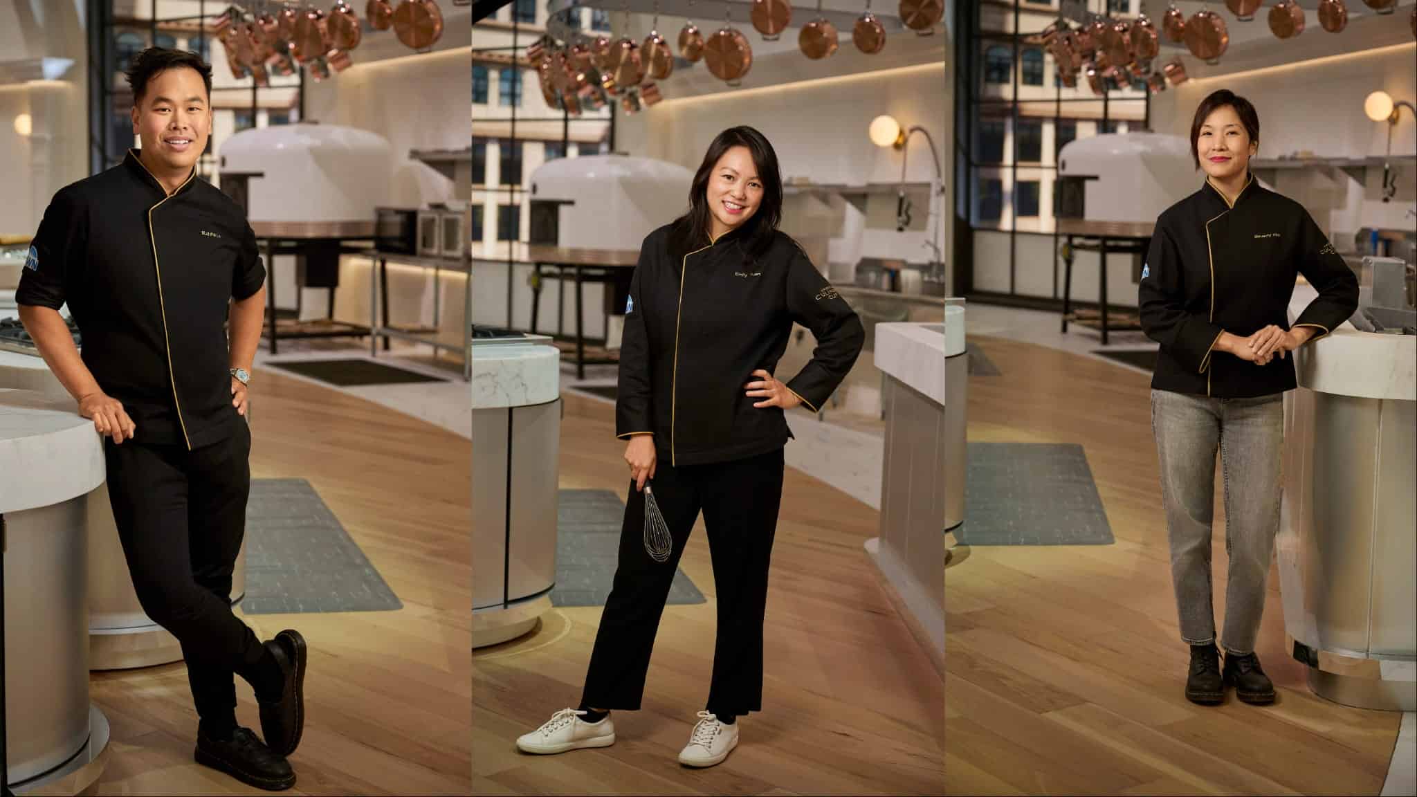 Three chefs in black uniforms pose in a modern, brightly lit kitchen. The kitchen features wooden floors, white counters, hanging copper pans, and large ovens in the background. Each chef stands confidently and smiles.