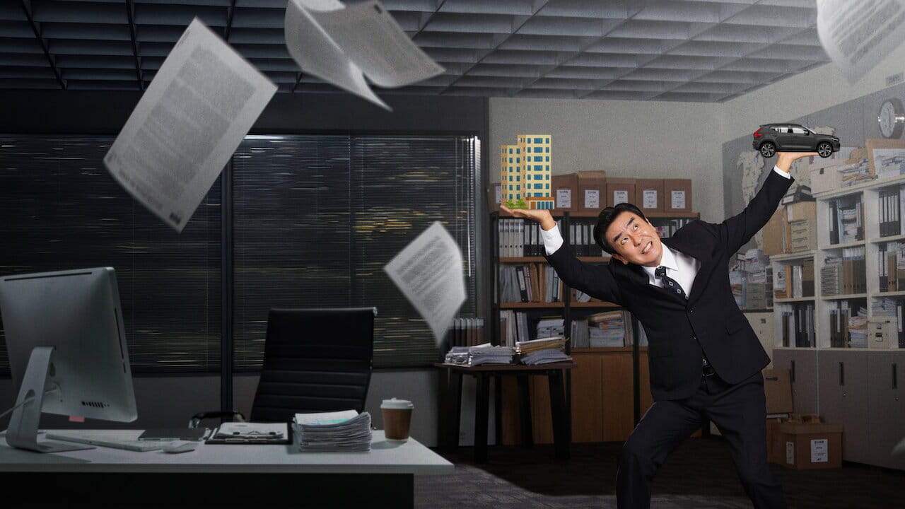 A man in a suit stands in a messy office, juggling a toy car and a model building while papers fly through the air, conveying chaos and multitasking.