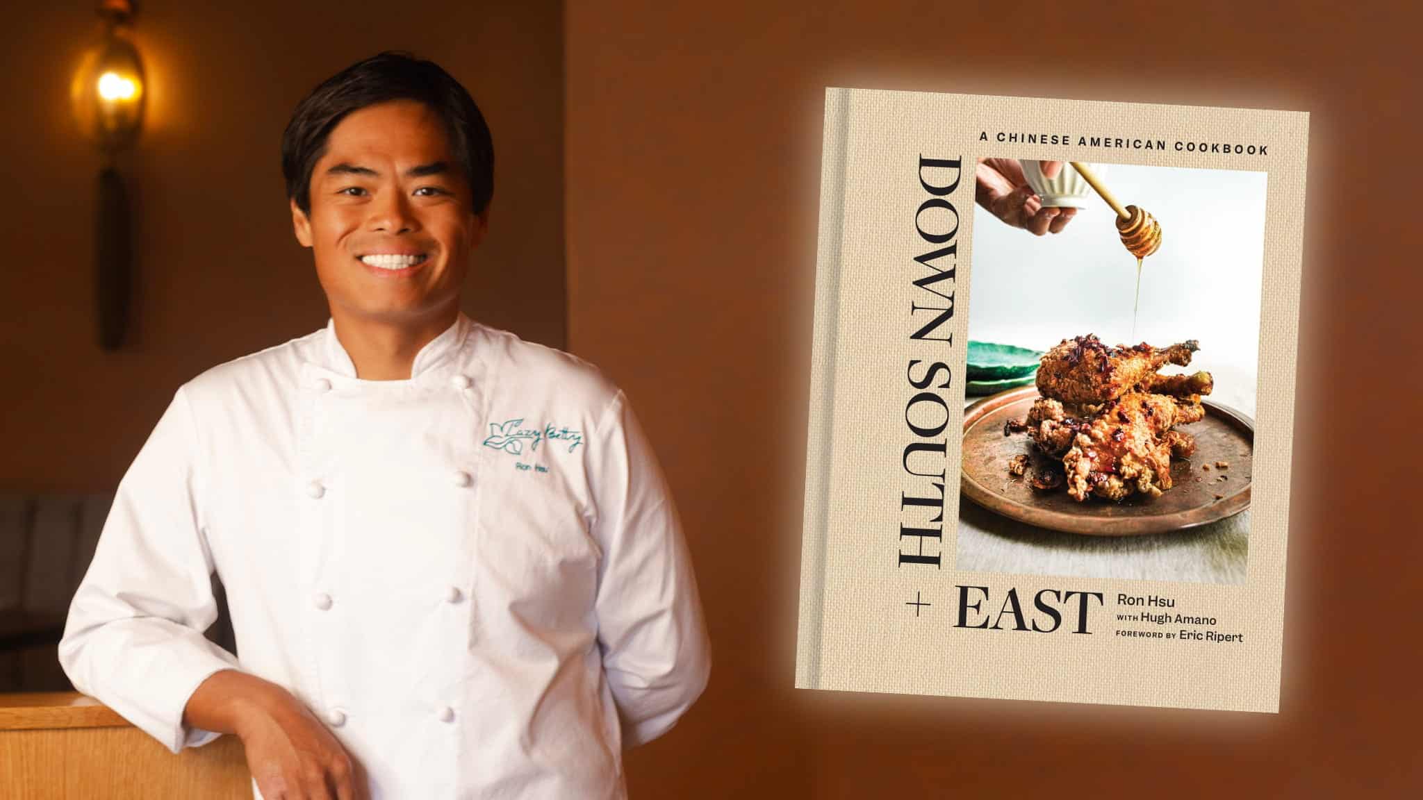 A smiling chef, Ron Hsu, in a white coat stands next to the cover of the cookbook Down South + East: A Chinese American Cookbook, which shows fried chicken being drizzled with honey on a plate.