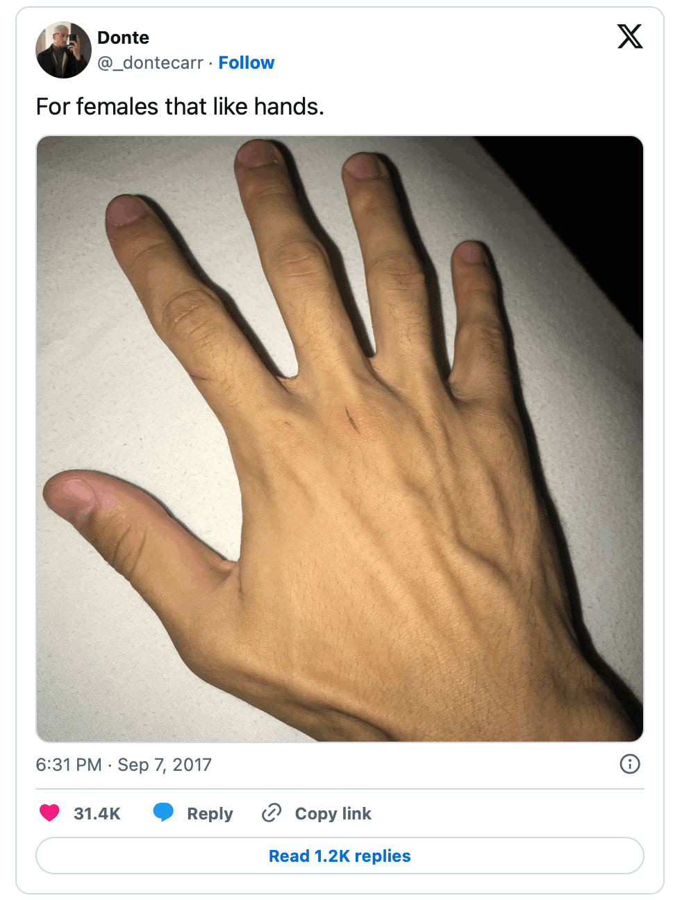 A close-up of a large hand with long fingers, resting on a white surface. The hand appears outstretched and is the main focus of the image.