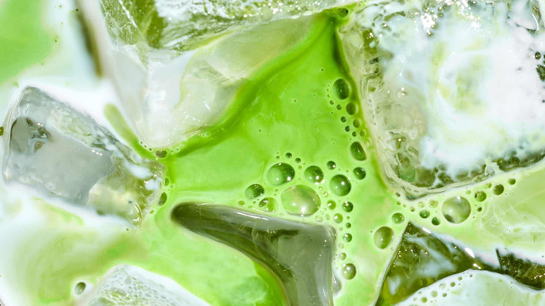 Close-up of ice cubes floating in a bright green liquid with frothy bubbles, creating a refreshing and vibrant appearance—perfect for celebrating National Matcha Day.