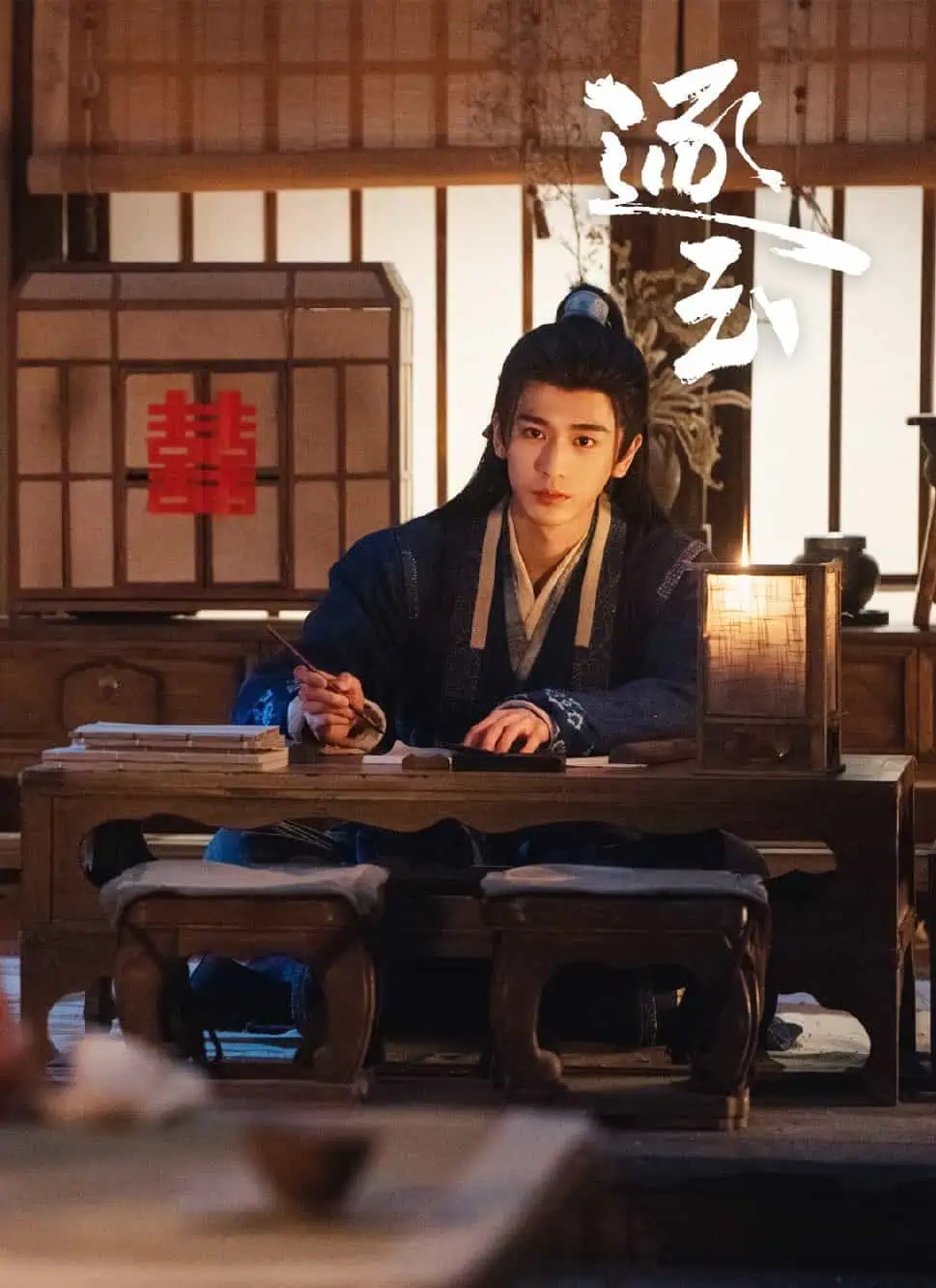 A woman in traditional Chinese attire, writes at a candle-lit table in the foreground while a man in blue traditional clothing sits at another table, looking at her in a warmly lit room with wooden decor.