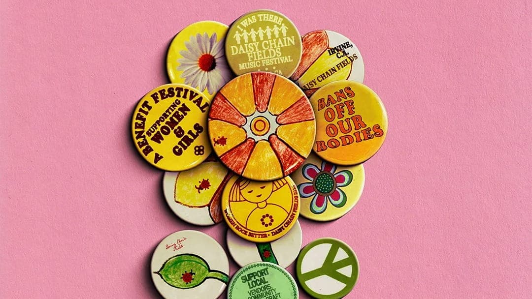 A cluster of vintage feminist and peace-themed buttons with slogans like Womens Festival, Mans Off Our Bodies, and Support Local, Think Global, arranged on a pink Daisy Fields background.