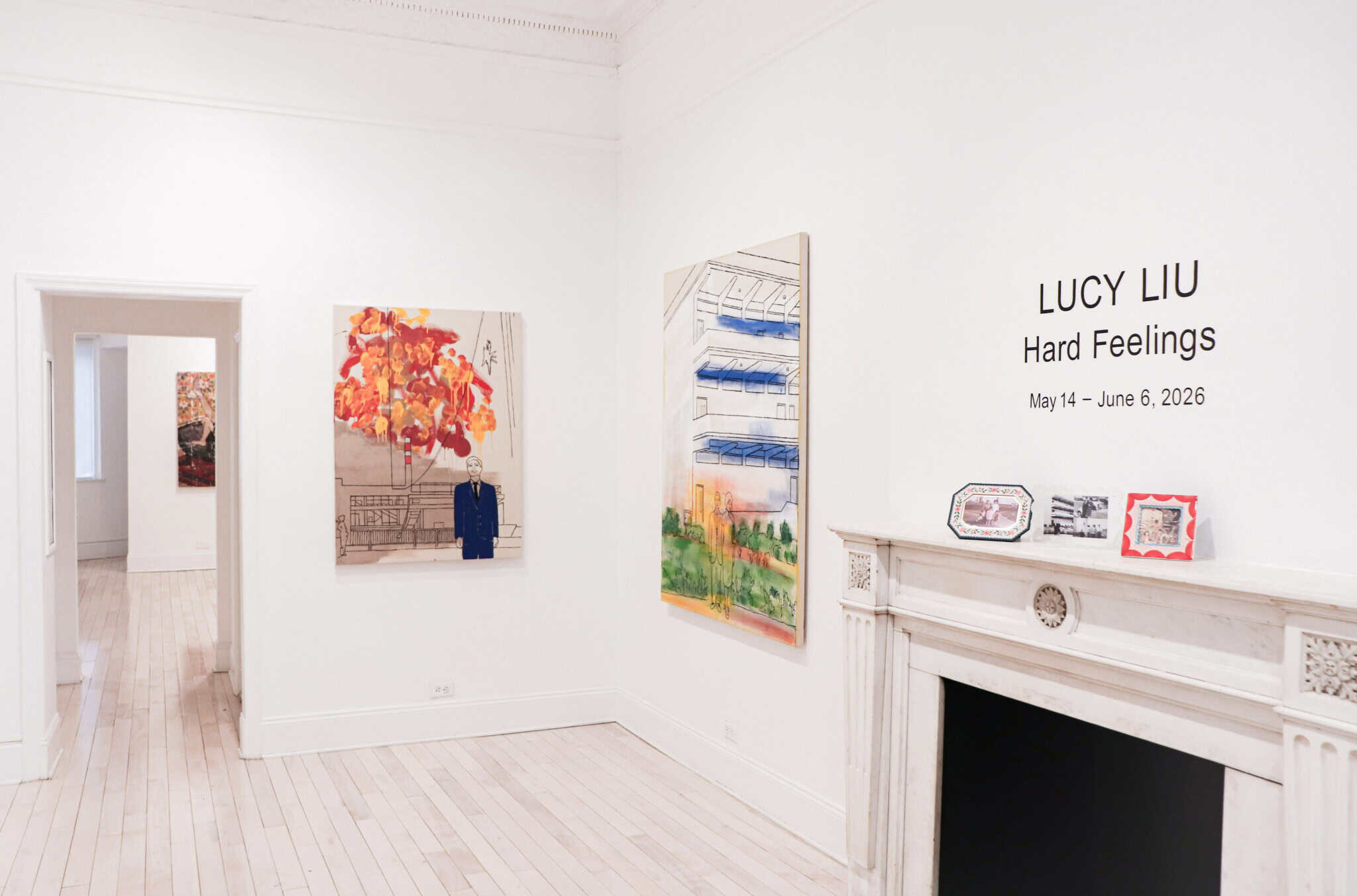 A bright art gallery displays colorful Lucy Liu art on white walls. Next to a marble fireplace, text reads: LUCY LIU Hard Feelings May 14 – June 6, 2026. Framed art sits elegantly on the mantel.