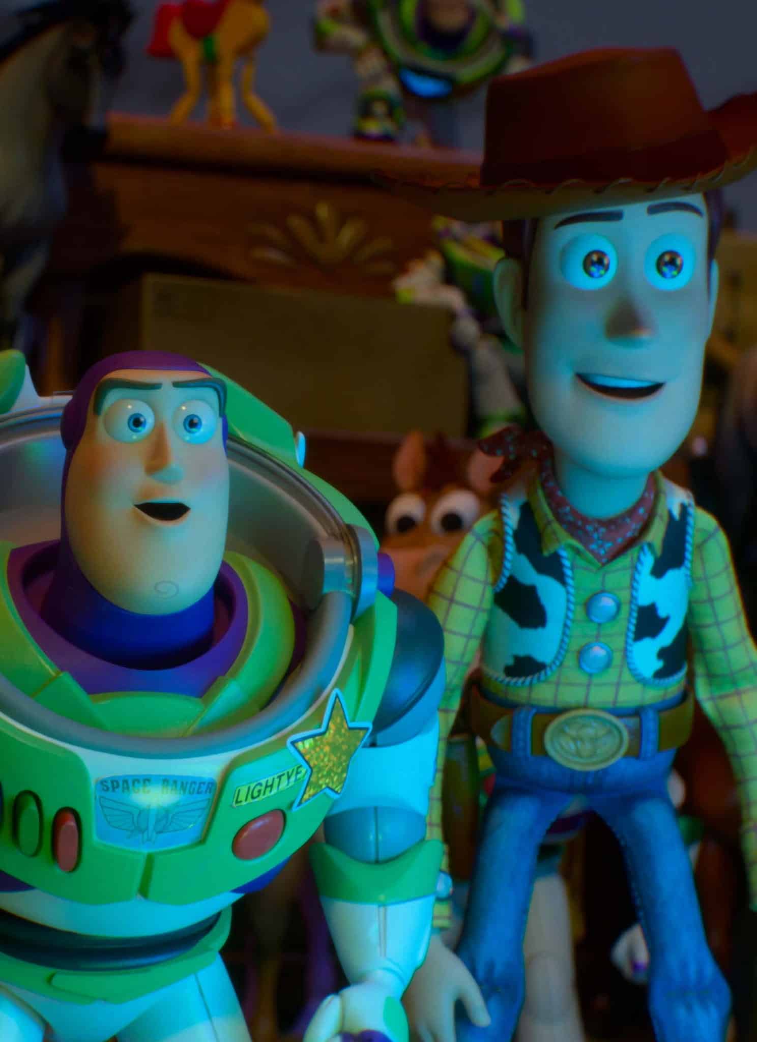 Three animated toy characters—a cowgirl, a space ranger, and a cowboy—stand together looking ahead with excited expressions. Other toy figures and colorful objects are visible in the background.