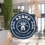 A round Azara Earth to Table logo is overlaid on a modern, sunlit restaurant interior with tall green plants, natural wood accents, and large windows.