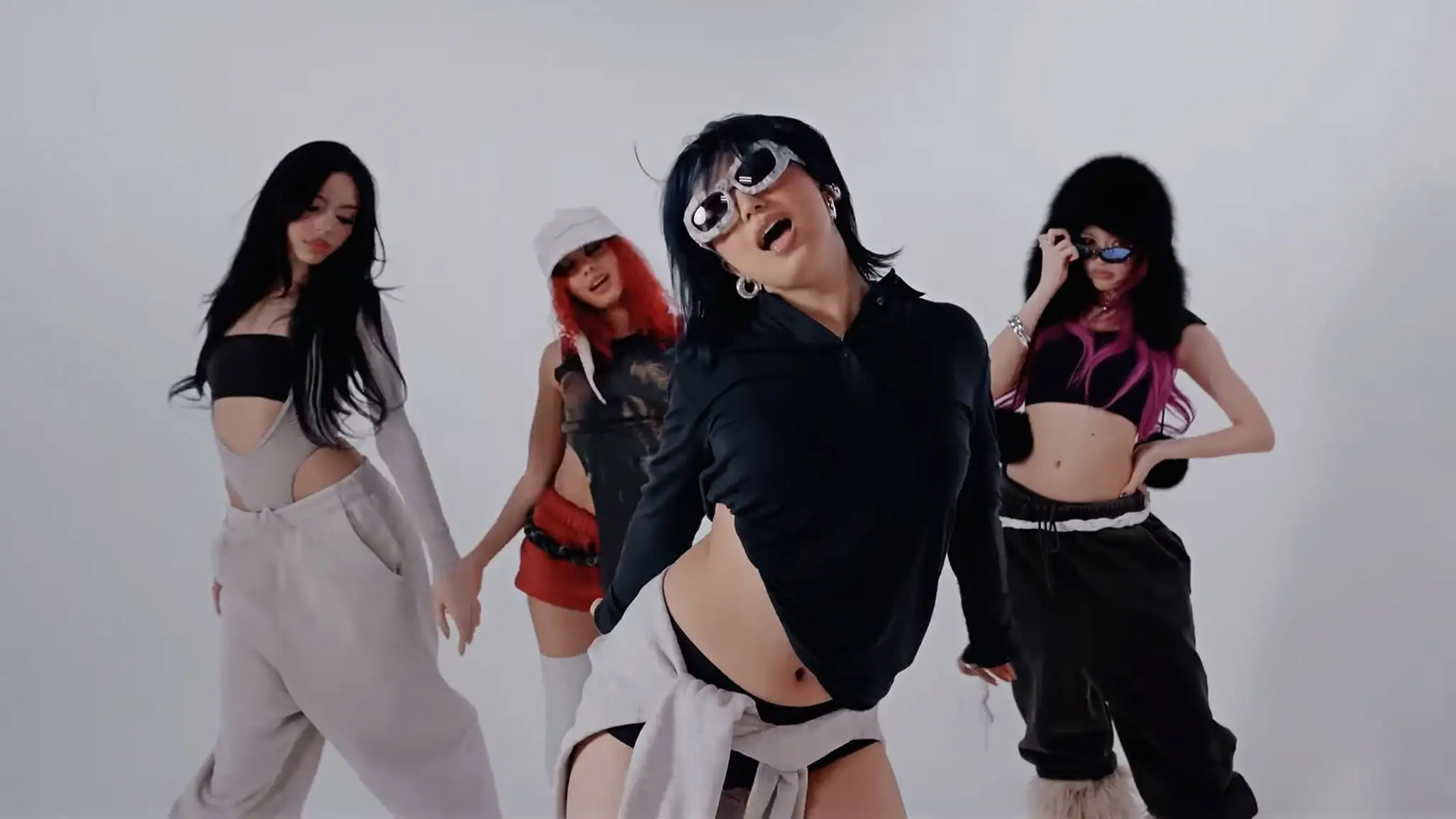 Four women pose stylishly in front of a plain white background, wearing fashionable streetwear outfits, sunglasses, and various accessories, exuding confidence and attitude.
