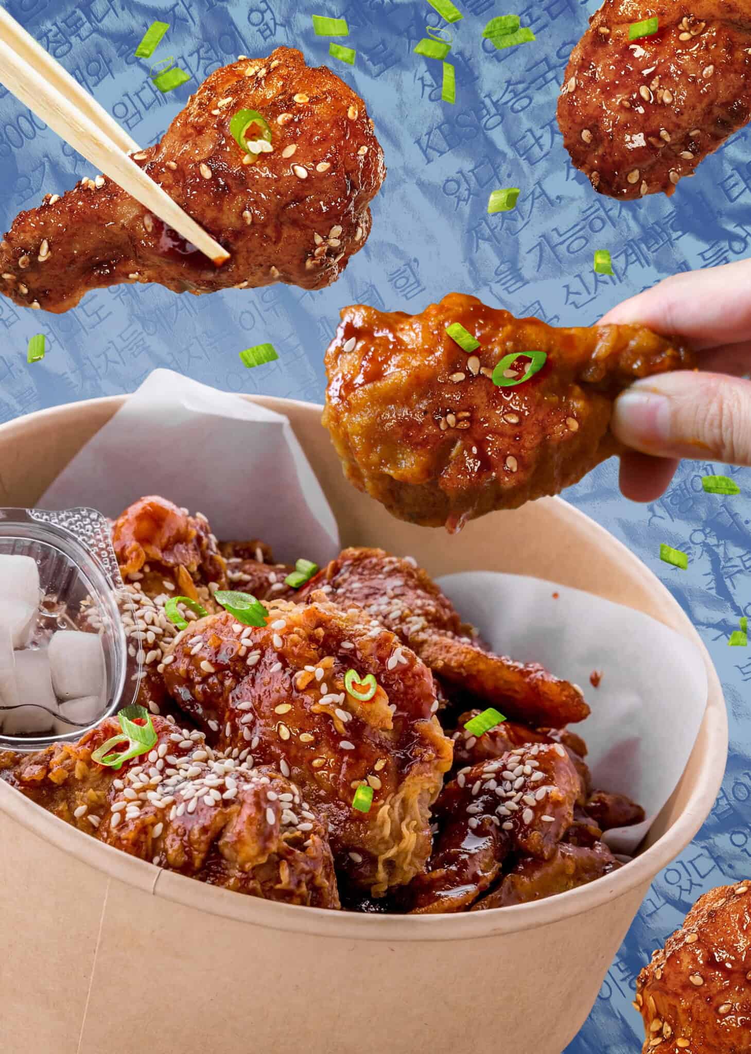 A hand holds a piece of saucy, sesame-coated Korean fried chicken above a box filled with more crispy pieces, garnished with green onions and served with pickled radish; patterned blue background with Korean text.