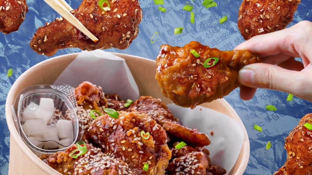 A hand holds a piece of saucy, sesame-coated Korean fried chicken above a box filled with more crispy pieces, garnished with green onions and served with pickled radish; patterned blue background with Korean text.