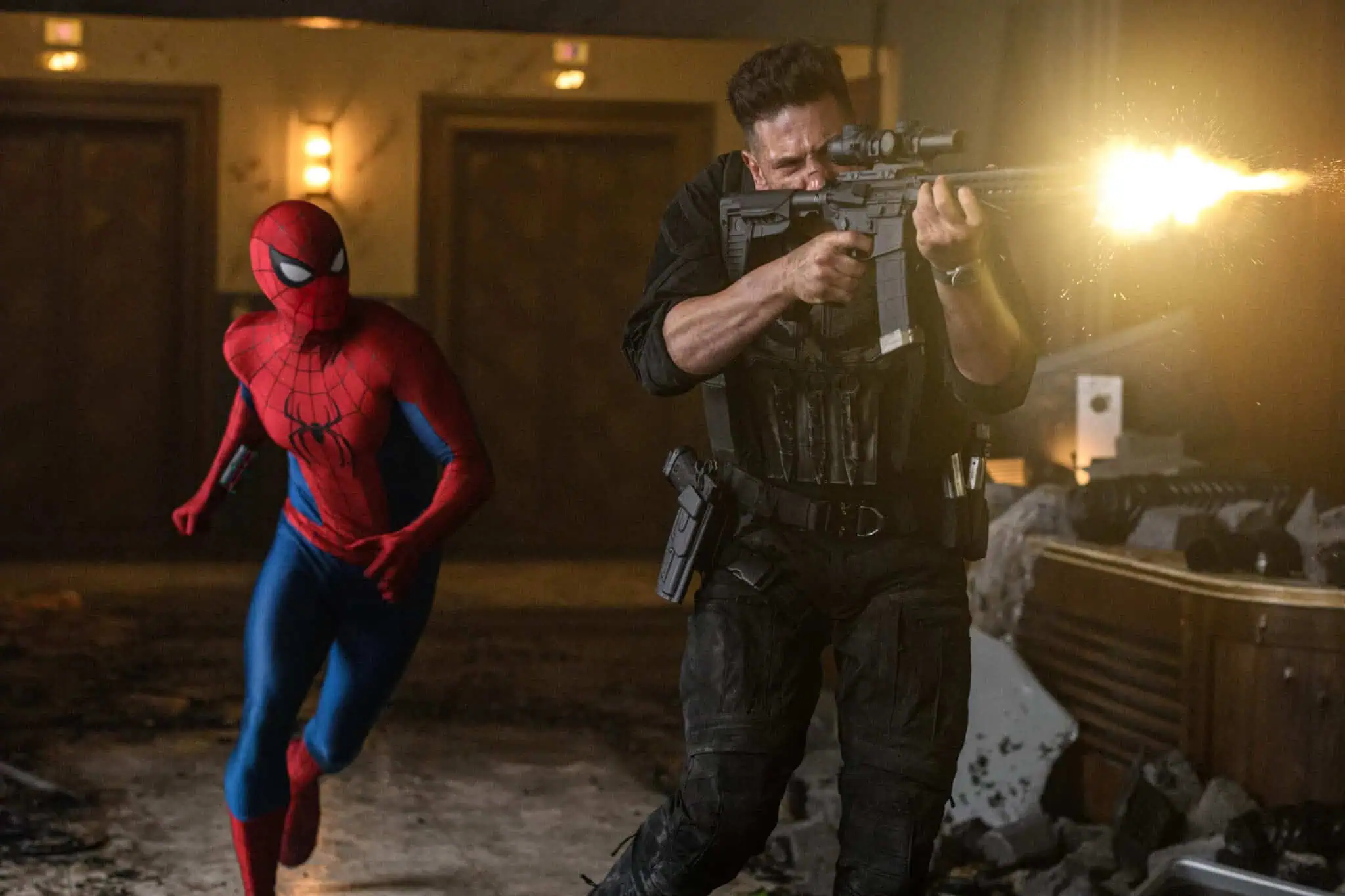 Spider-Man runs beside a man in tactical gear firing a rifle in a damaged, dimly lit room. Debris and bullet holes are visible, adding to the chaotic scene.