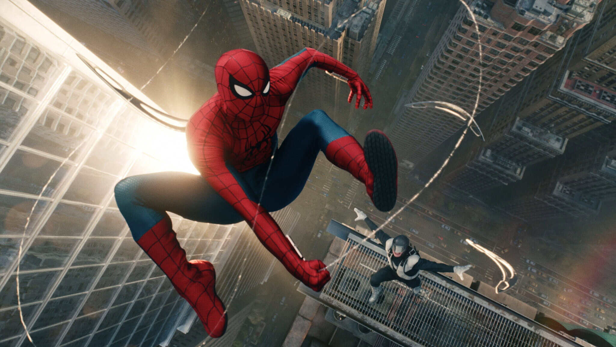 Spider-Man swings high above a city, with skyscrapers below him. Another costumed character leaps nearby, both appearing in action mid-air.